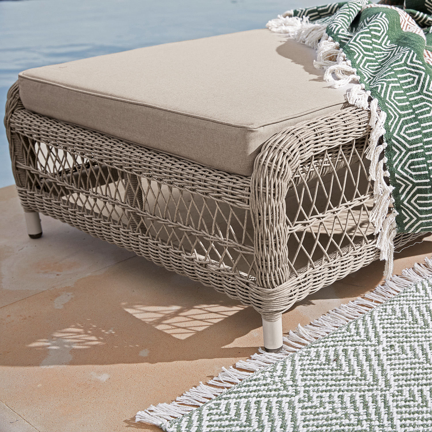 Beiger Rattan-Hocker mit weichem Polster und grünem Deckenmuster auf Terrasse