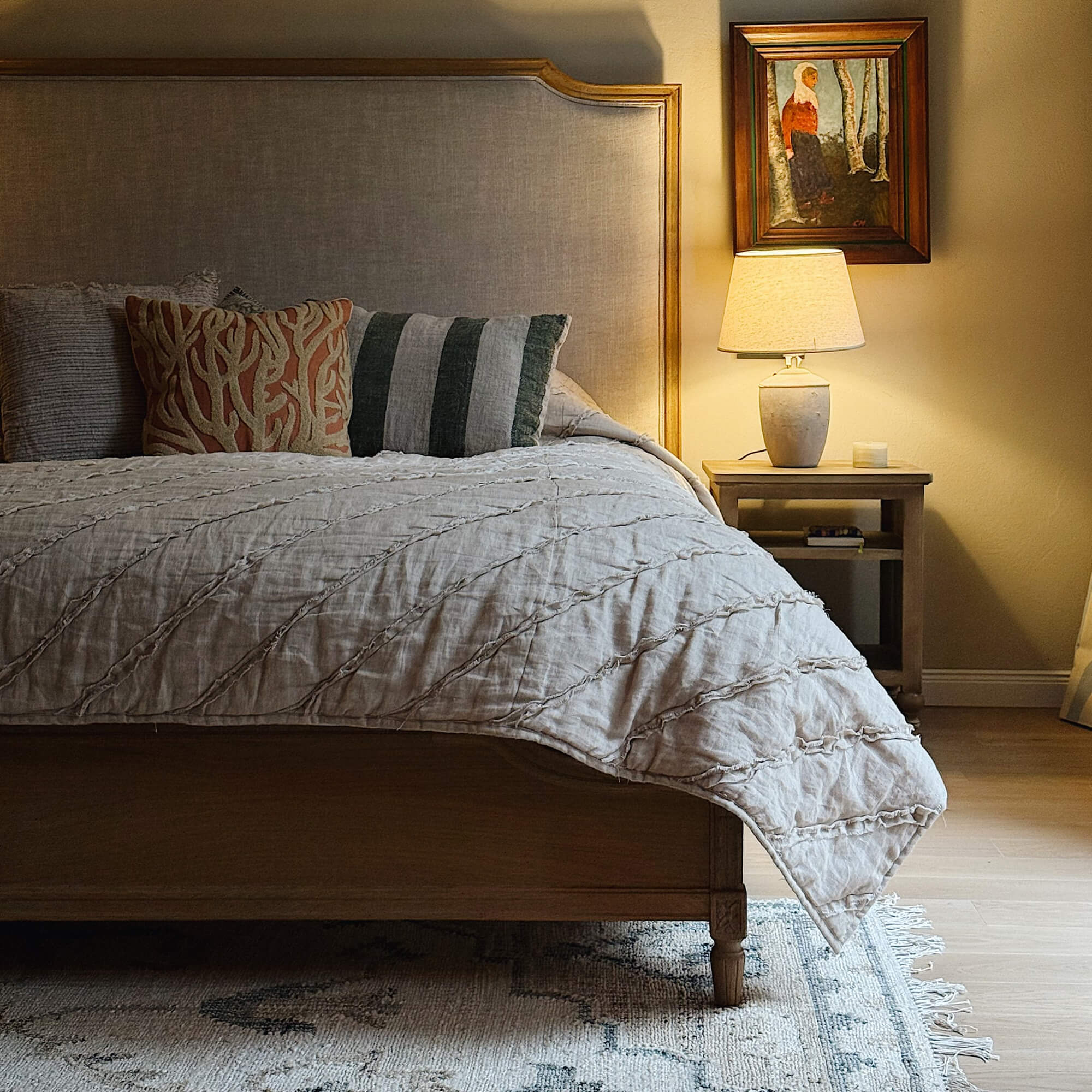 Gemütliches Schlafzimmer mit Holzbett, beiger Tagesdecke und Lampe auf Holz-Nachttisch