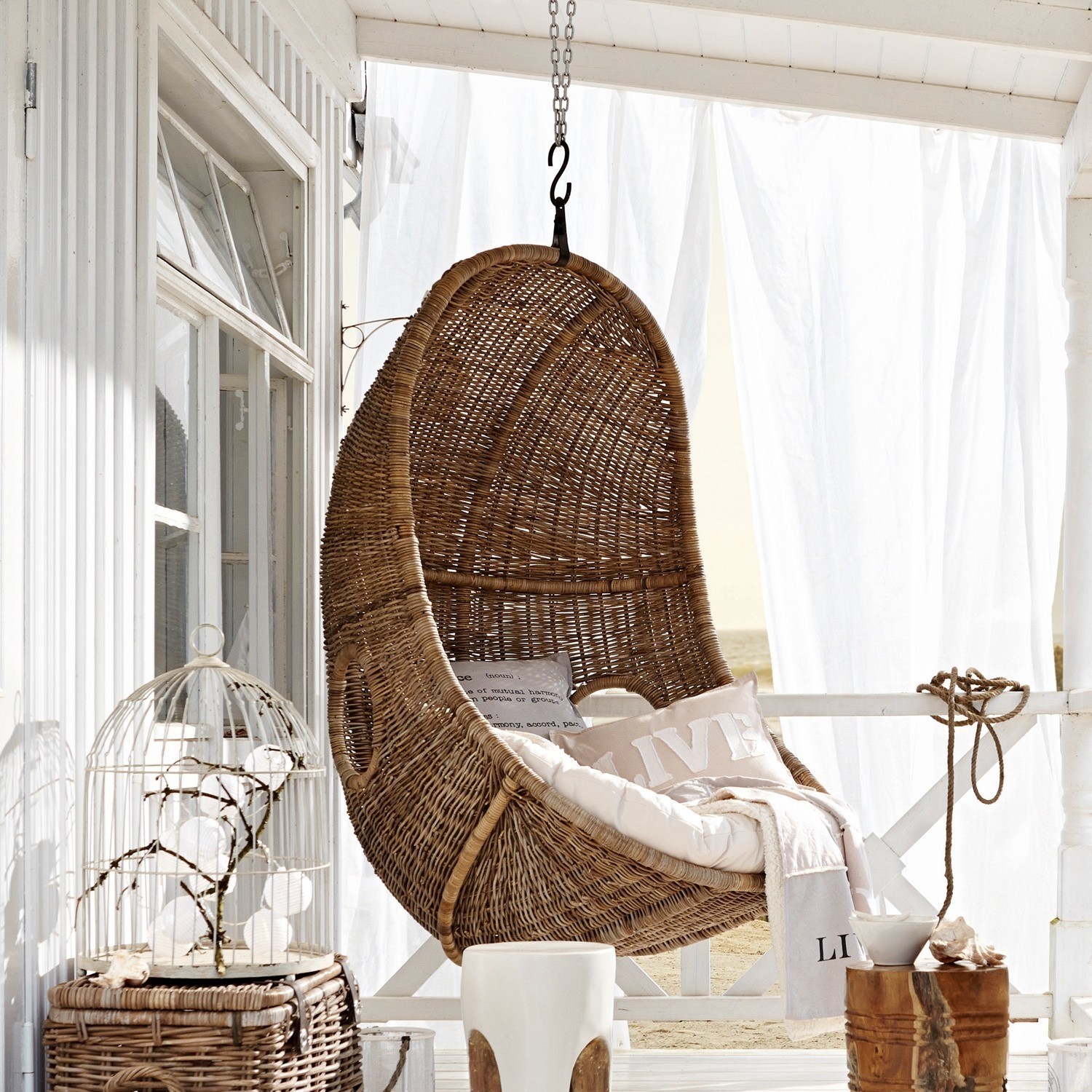 Hängesessel aus natürlichem Rattan mit Kissen und Decke auf Terrasse mit Strandblick