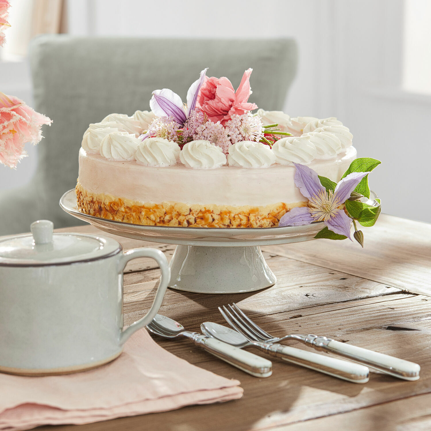 Platte Biarré Kuchen auf Keramik-Tortenplatte mit Creme und Blumen, weiße Besteckgriffe auf Holztisch
