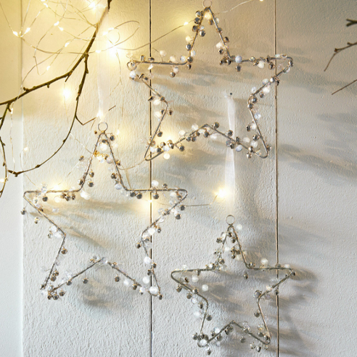 Dekorative Metallsterne mit weißen Glöckchen und LED-Lichtern als Weihnachtsdeko an Wand