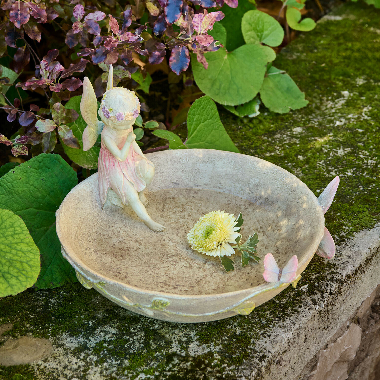 Dekorative Gartenschale mit Feenfigur und pastellfarbenen Schmetterlingen auf Steinmauer