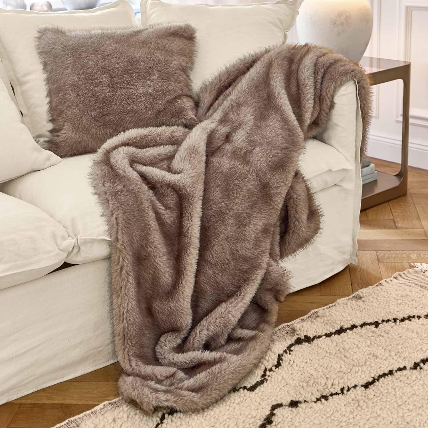 Weiche braune Kunstfell-Decke und Kissen auf weißem Sofa in gemütlichem Wohnzimmer