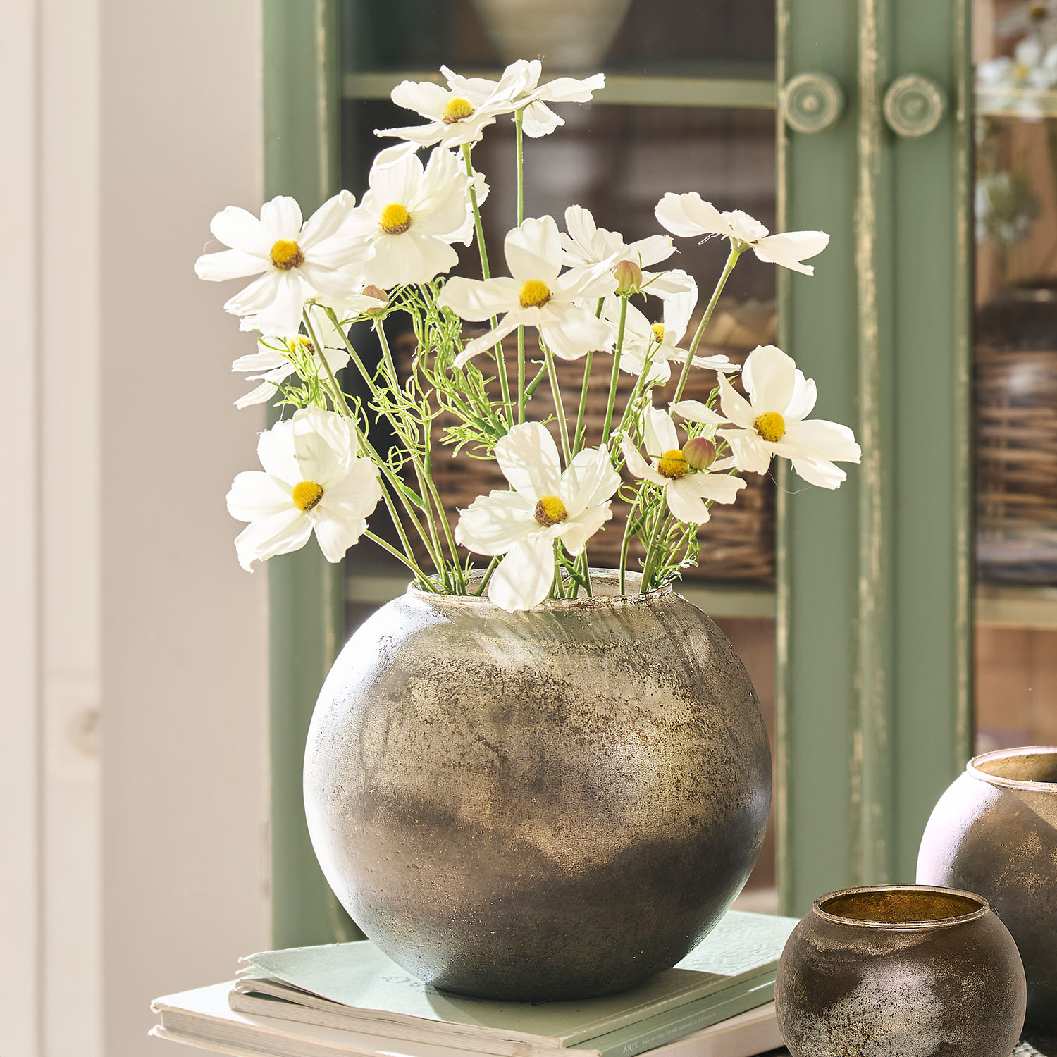 Runder silberner Metallvase mit weißen Blumen auf Büchern, stilvolle Wohnraumdekoration