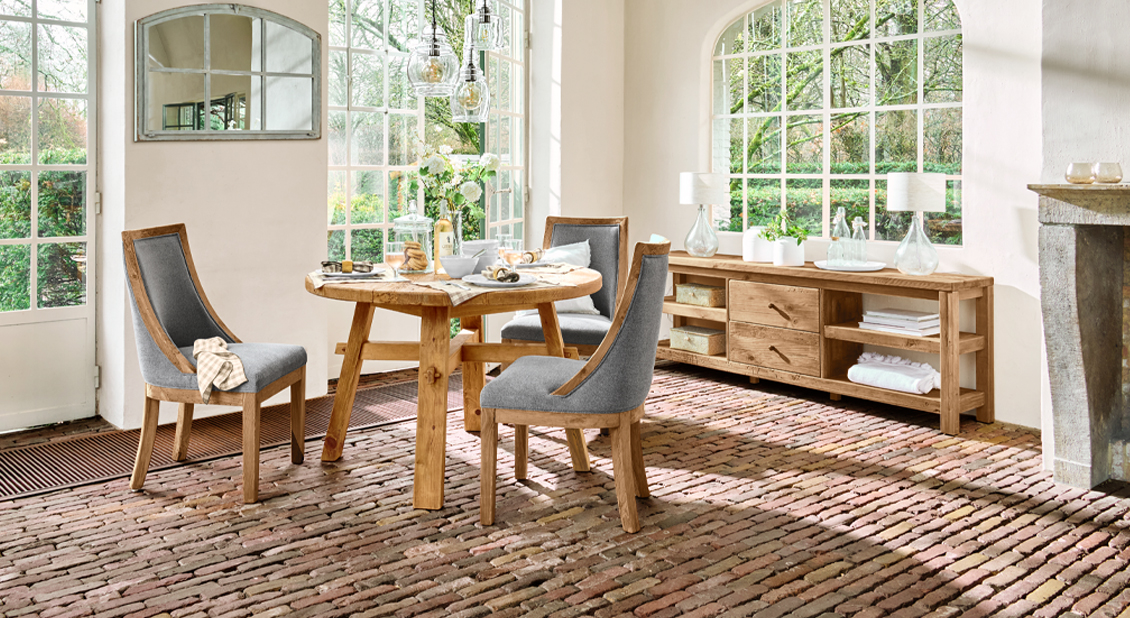 Rustikaler Essbereich mit Holztisch und grauen Polsterstühlen auf Ziegelboden im Landhausstil