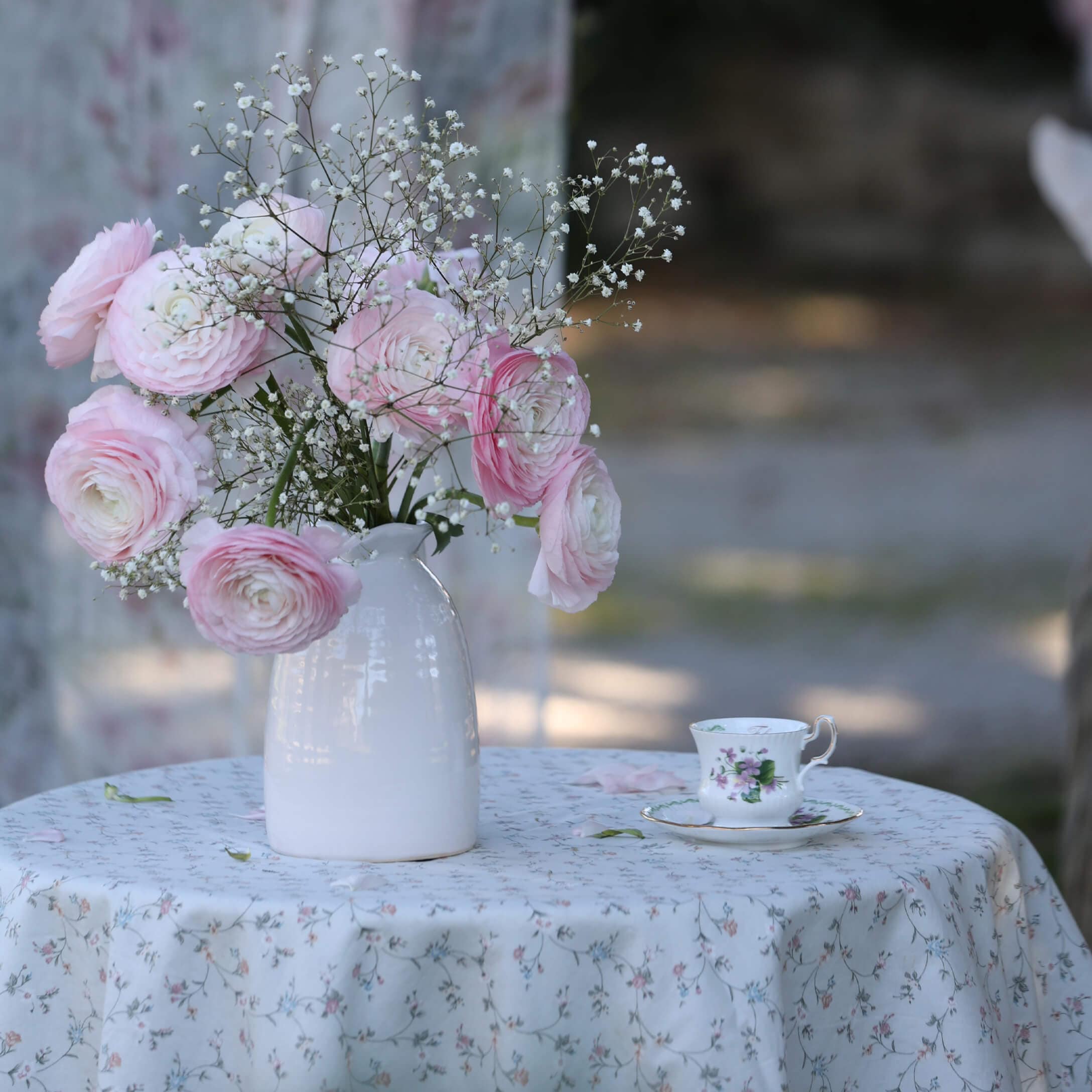 Strauß aus rosa und weißen Blumen in weißem Keramikvase auf Tisch mit floralem Tischtuch
