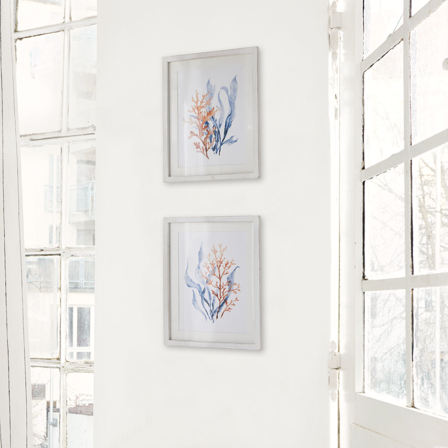 Zwei weiße Bilderrahmen mit blauen und orangen Meerespflanzenmotiven an weißer Wand