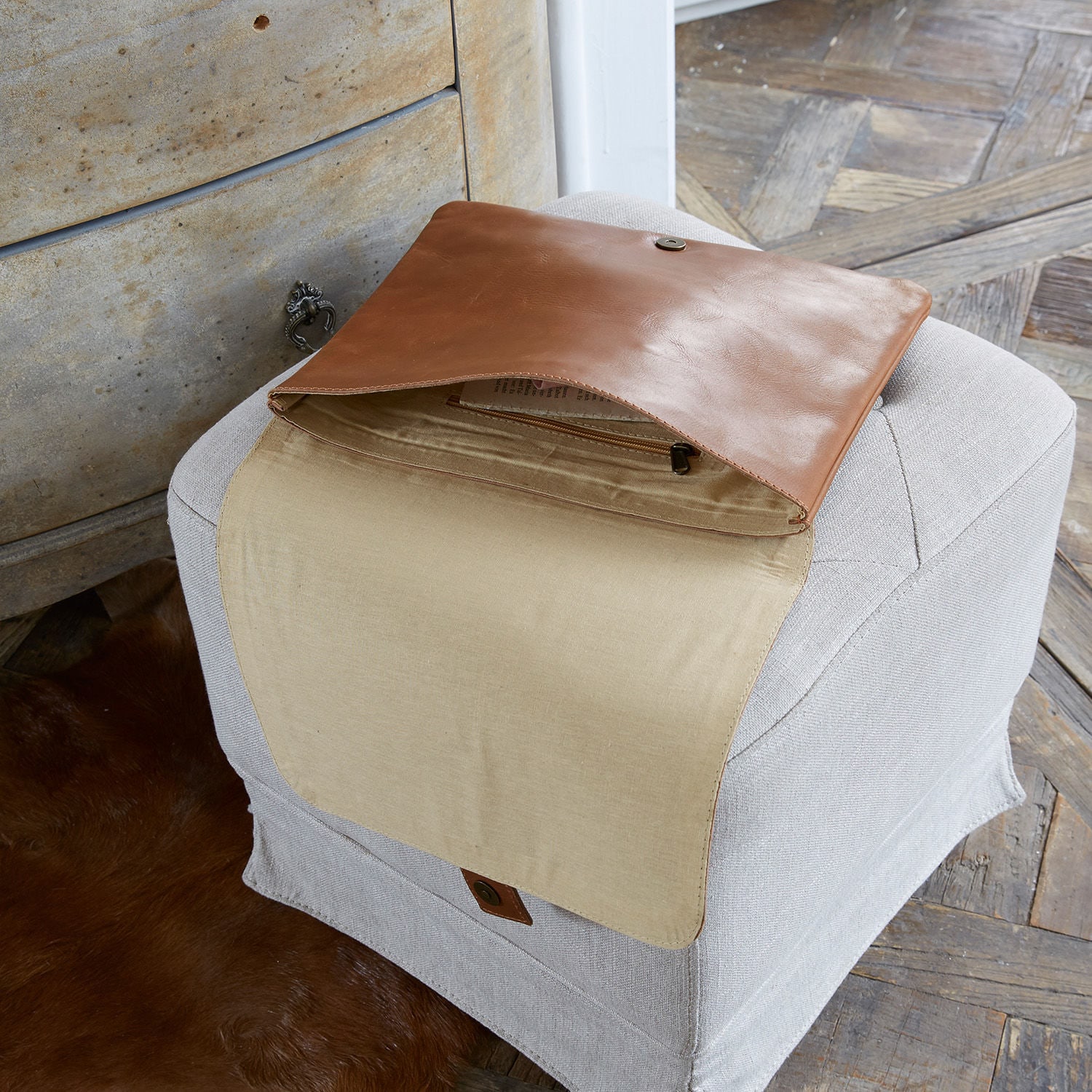 Braune Lederhandtasche mit beigem Innenfutter auf hellgrauem Hocker in Holzraum