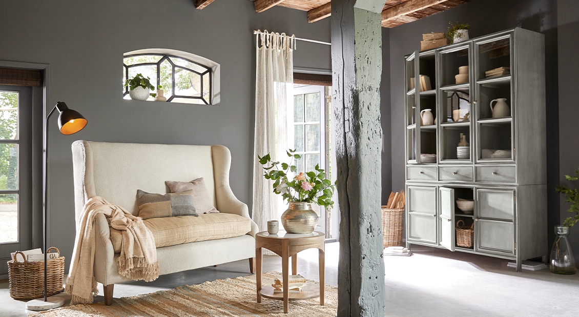Gemütliches Wohnzimmer mit grauem Holzvitrinenschrank und cremefarbenem Sofa auf Holzbeinen, natürliche Dekoration