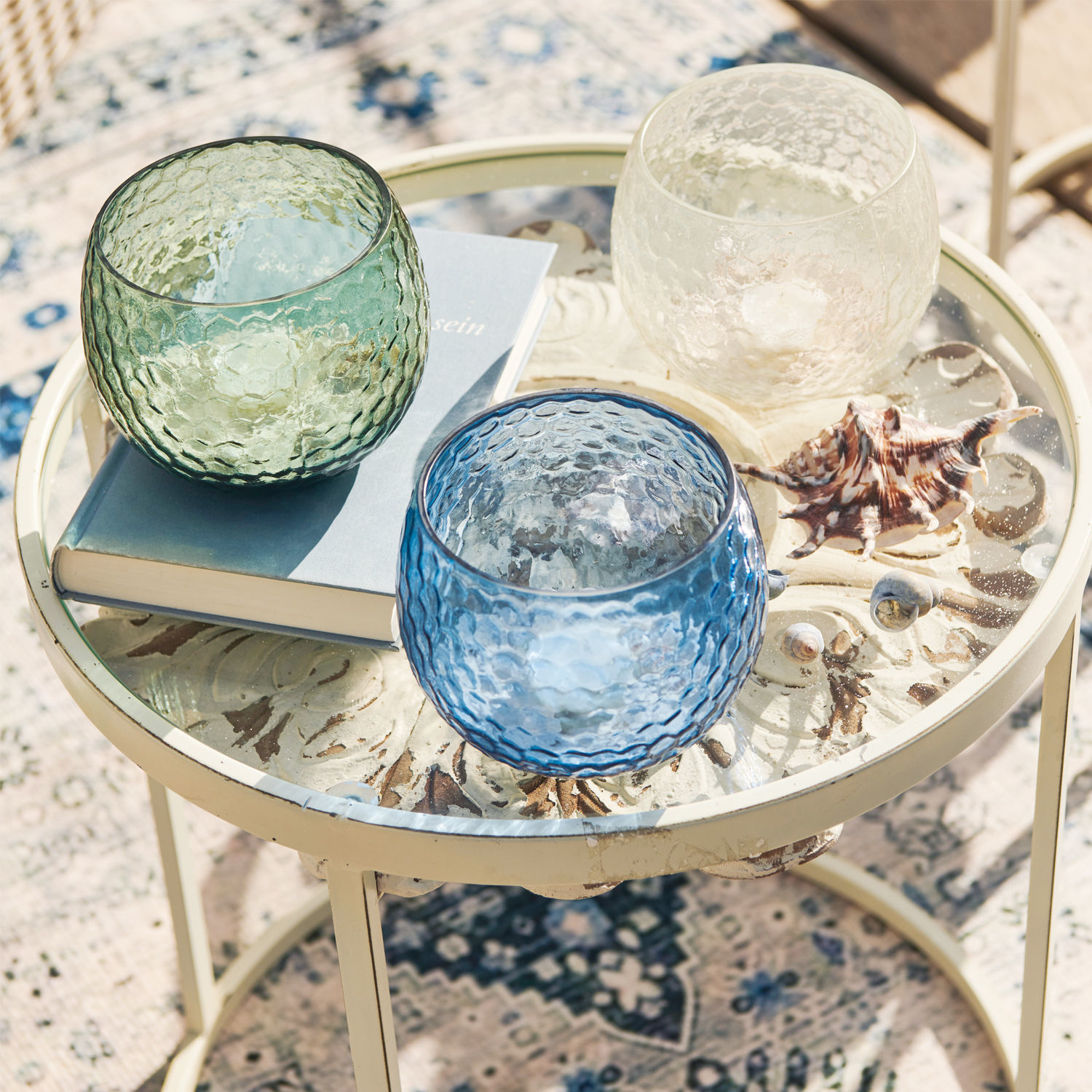 Drei bunte Glas-Teelichthalter in Grün, Blau und Transparent auf einem Glastisch