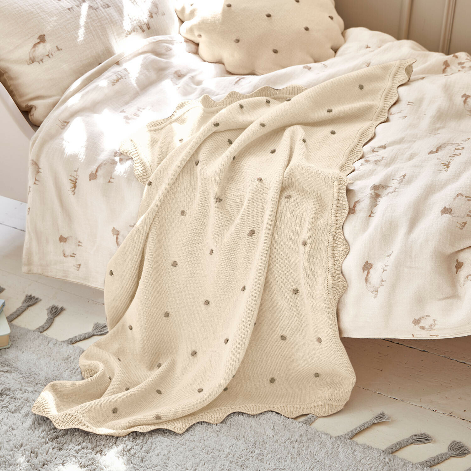 Plaid Saphie Beige gestrickte Decke mit grauen Punkten auf Bett mit hellem Bettzeug und natürlichem Kissen