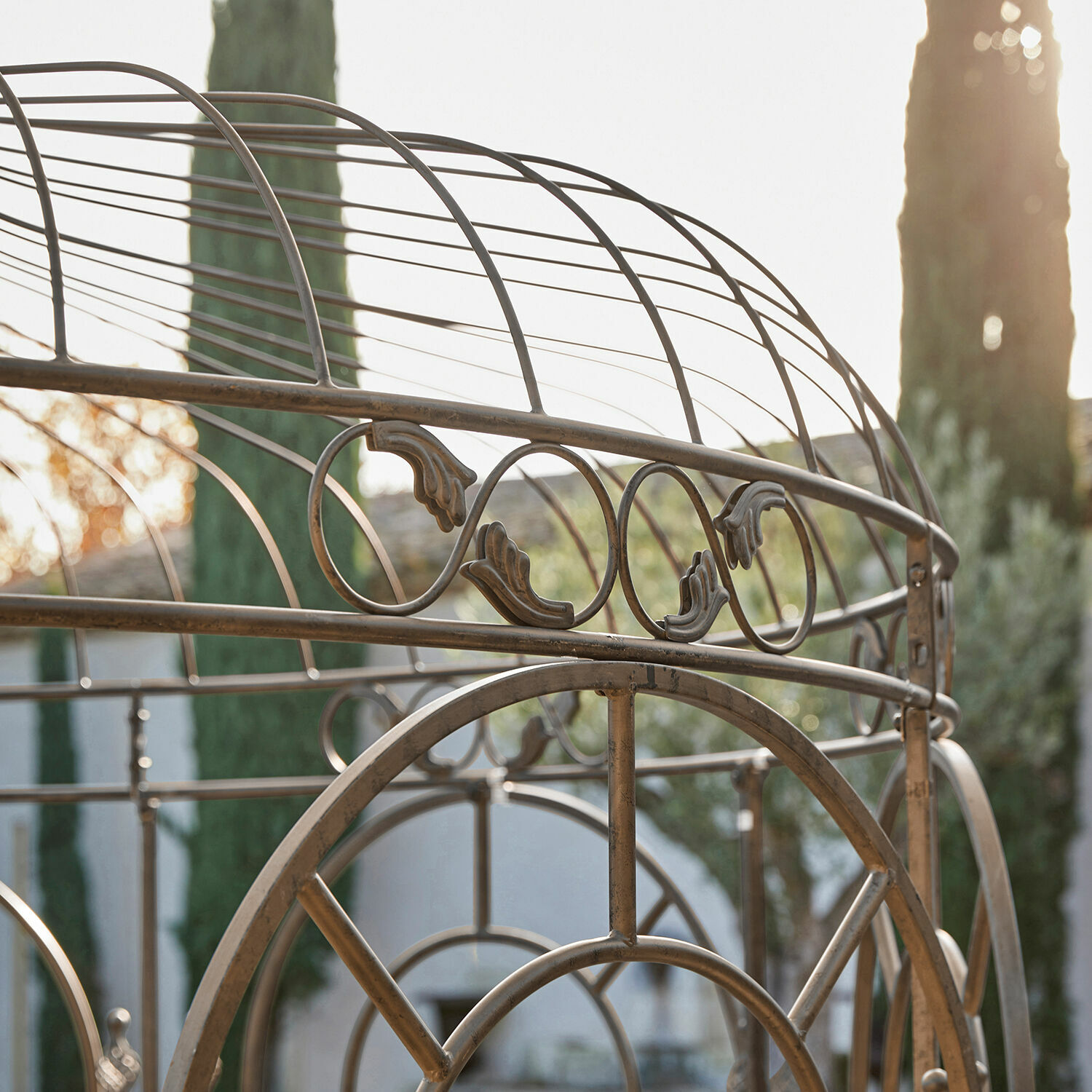 Metallstruktur mit dekorativen Vintage-Details vor Garten und Sonnenlicht