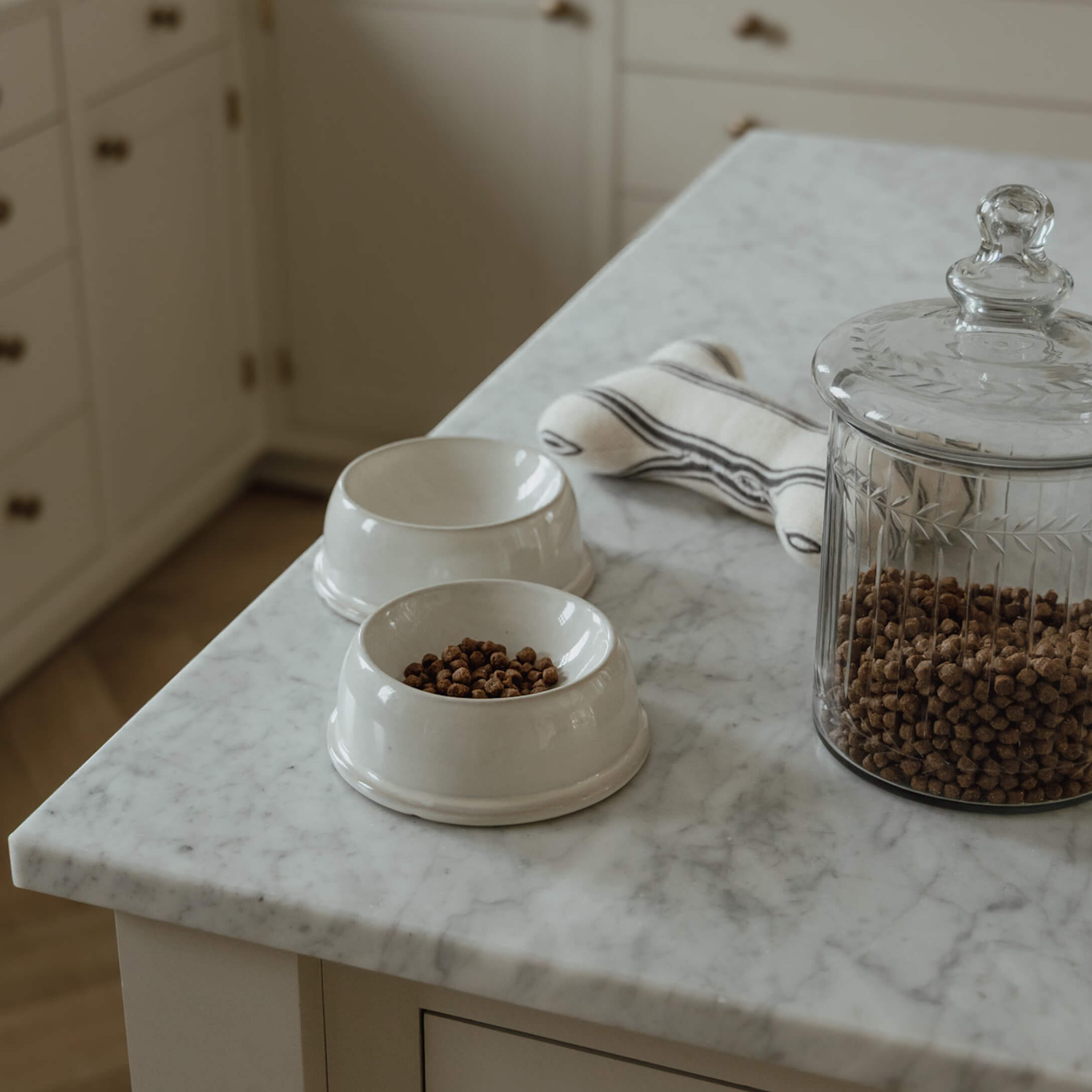 Weiße Keramikfutternäpfe mit Trockenfutter und Glasbehälter auf Marmorarbeitsplatte in Küche