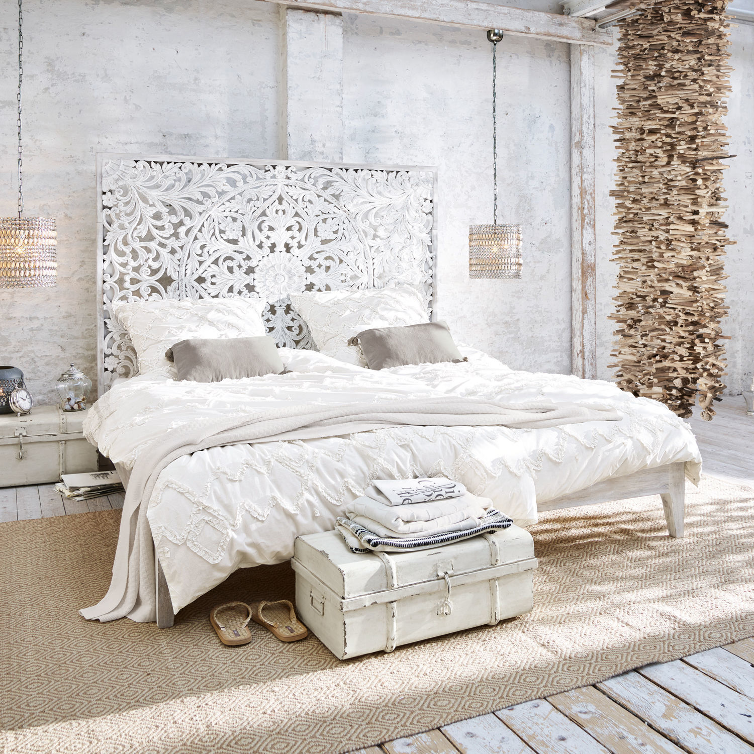 Schlafzimmer mit weißem Bett, geschnitztem Holz-Kopfteil und heller Boho-Bettwäsche