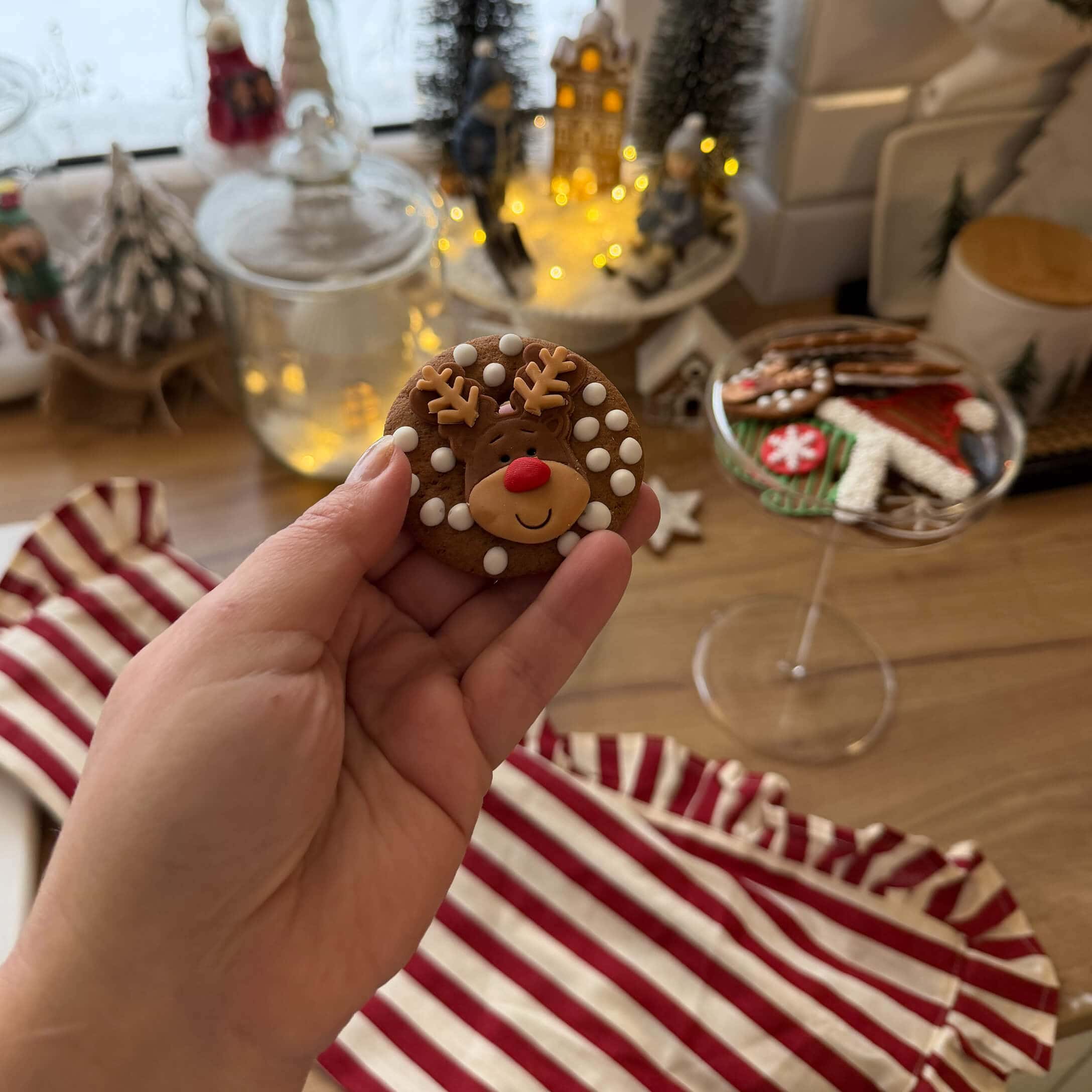 Hand hält Lebkuchen mit Rentier und weißen Punkten vor weihnachtlicher Dekoration und Keksen