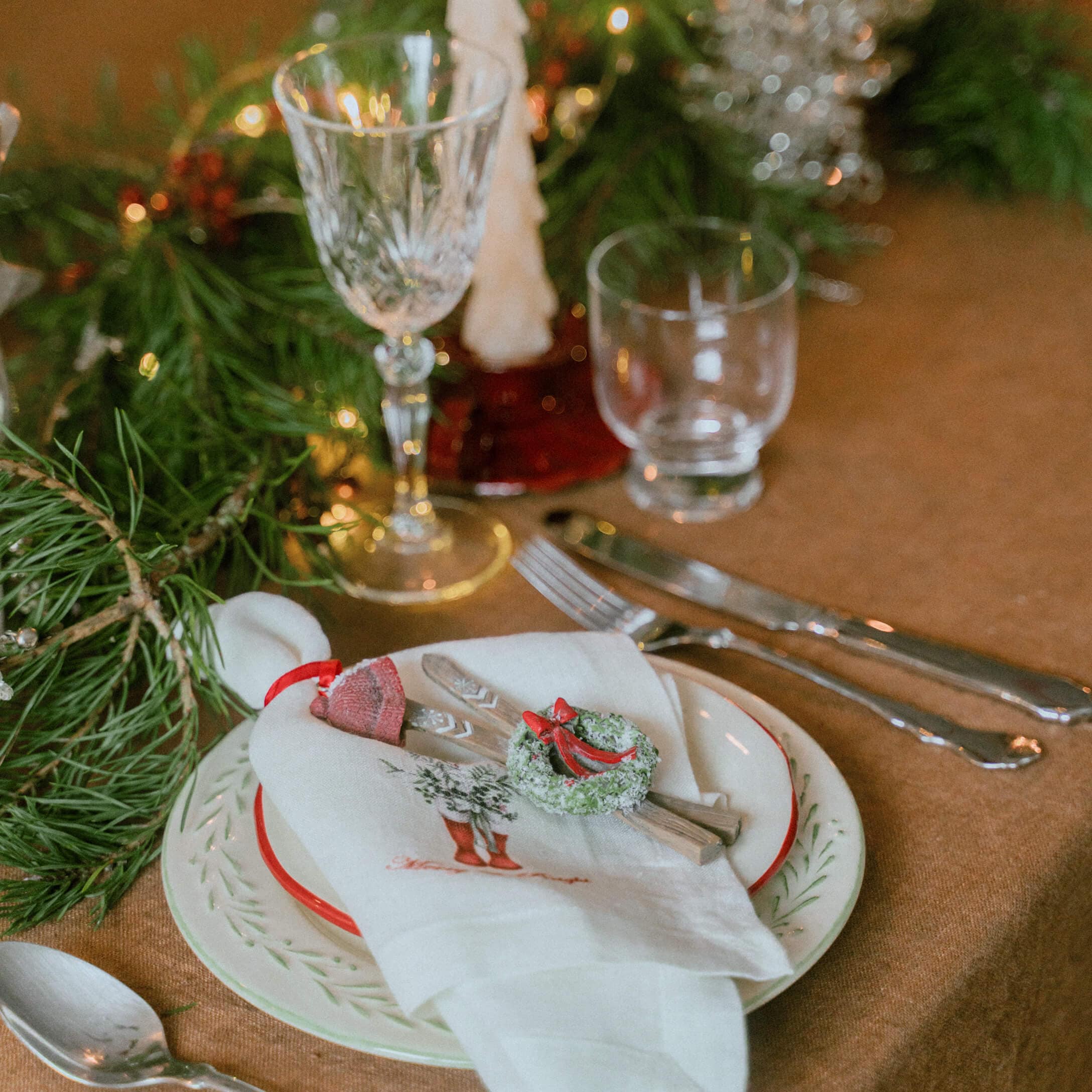 Weihnachtliche Tischdekoration mit weißem Leinenserviette, grünen Zweigen und kleinem Kranz als Deko