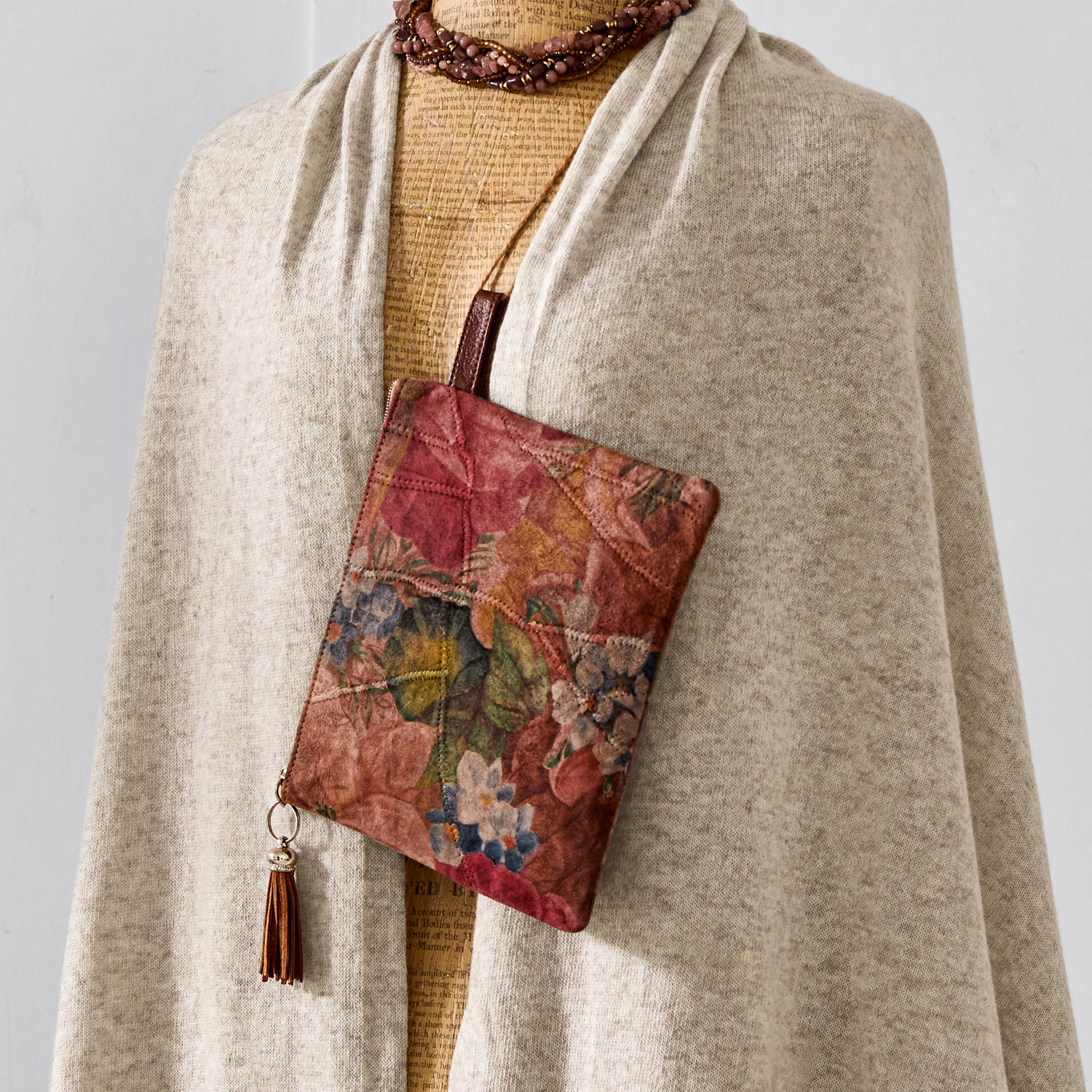 Kleine Tasche aus weichem Leder mit floralem Muster und braunem Quaste vor hellem Hintergrund