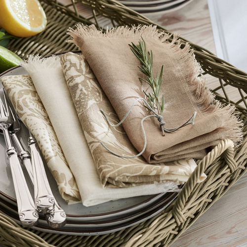 Set aus Leinen-Servietten in natürlichen Beigetönen auf einem geflochtenen Tablett für Tischdeko