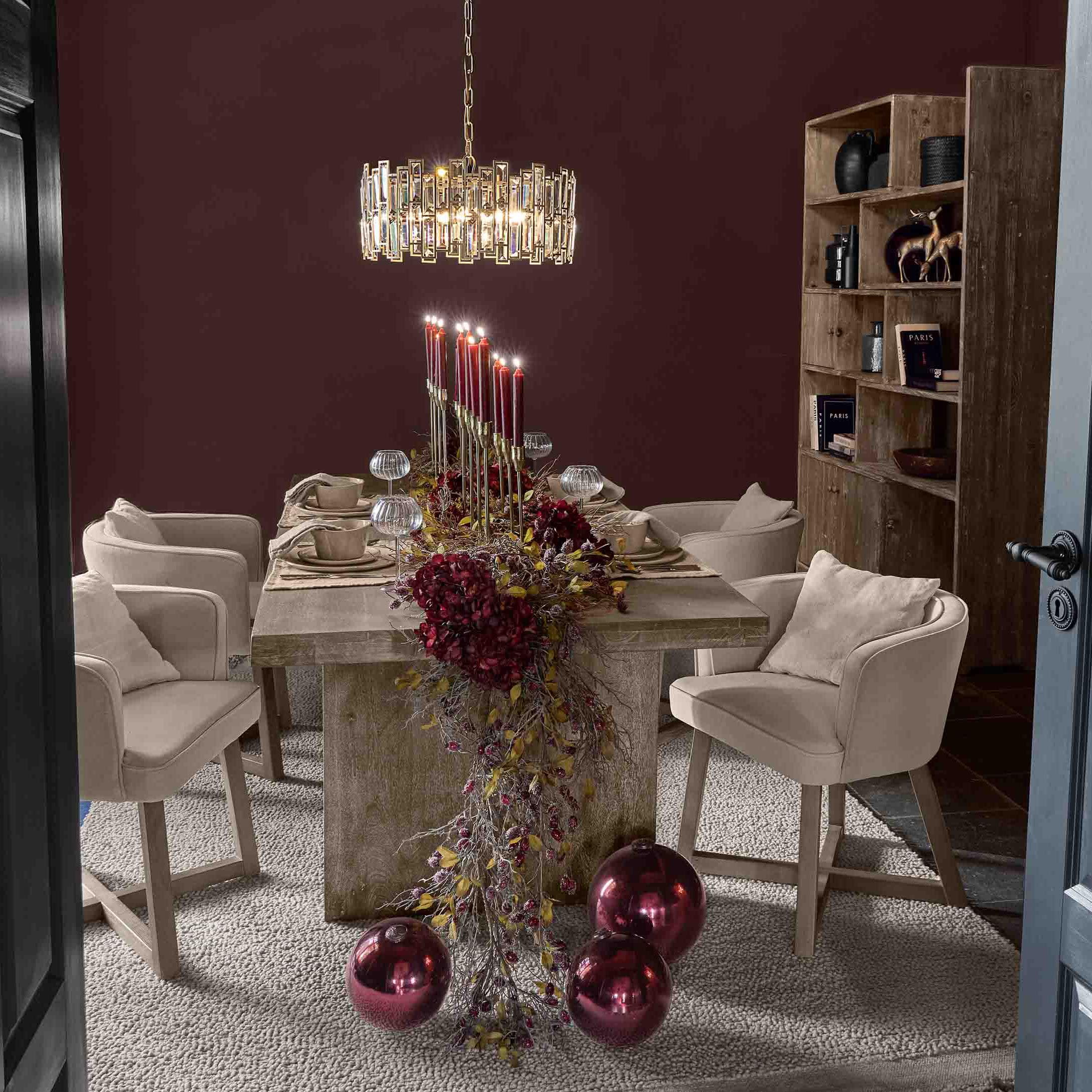 Esszimmer mit Holztisch, beigen Stühlen und roter Kerzen- sowie Weihnachtskugel-Dekoration