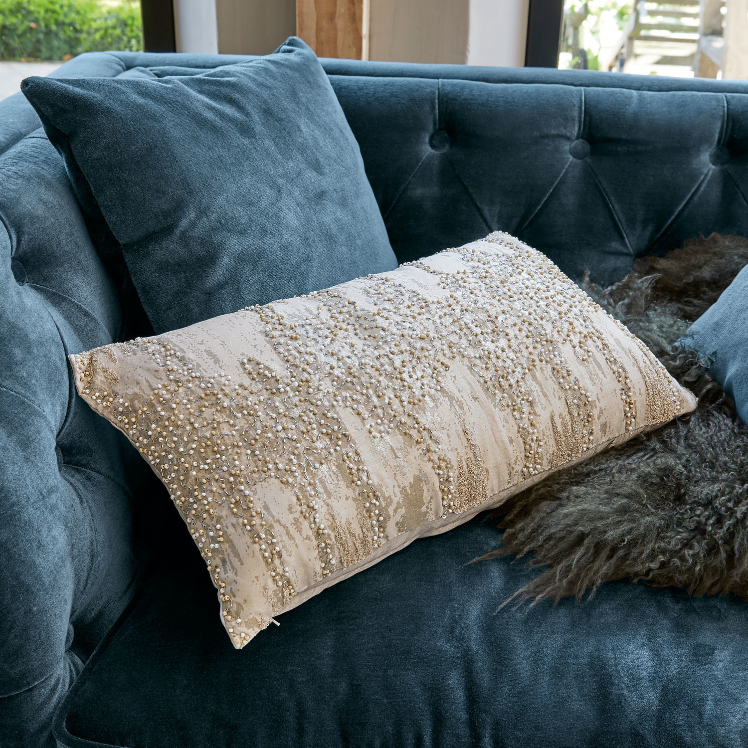 Beige dekoratives Kissen mit Perlen auf blauem Samtsofa, stilvolles Wohnaccessoire