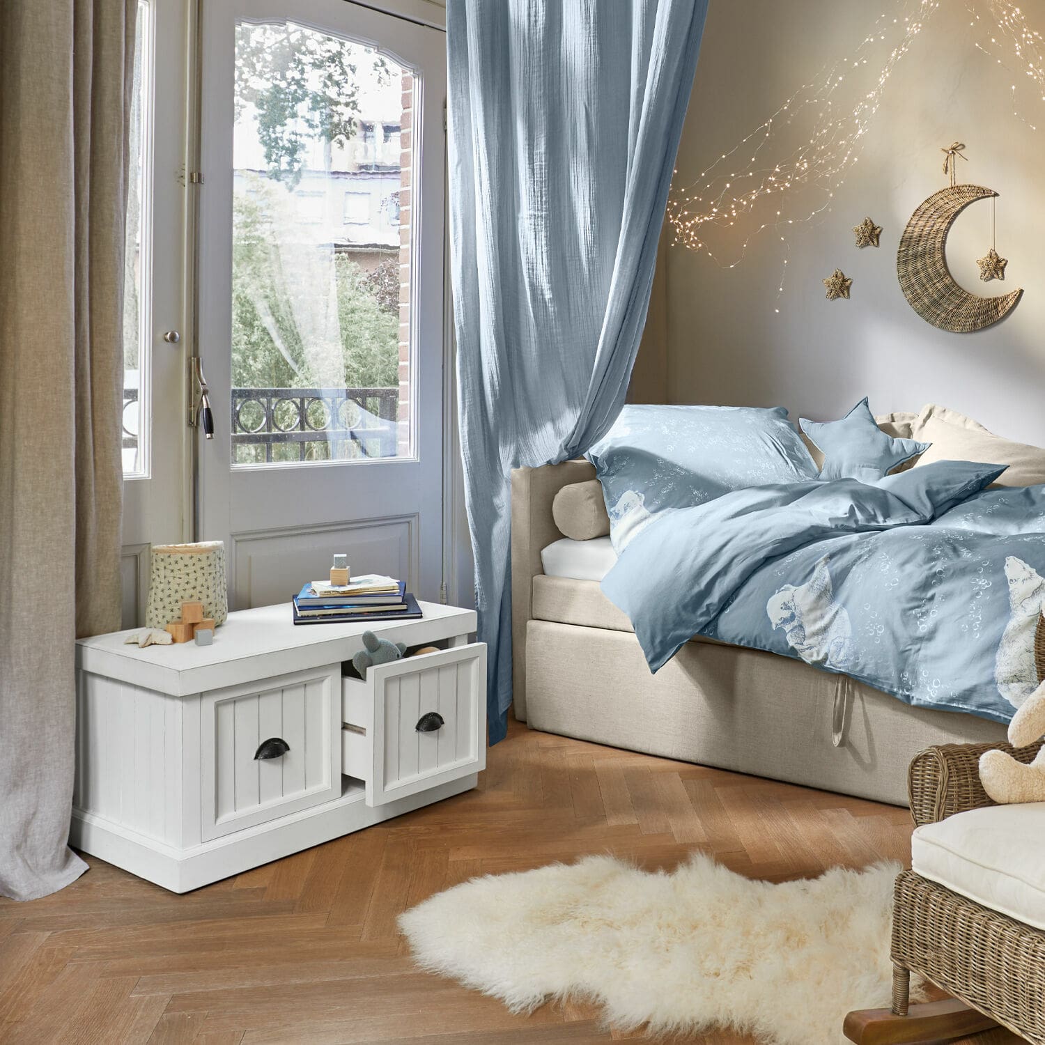 Weiße Holzkommode mit Schubladen in gemütlichem Zimmer mit blauer Bettwäsche und Wanddeko