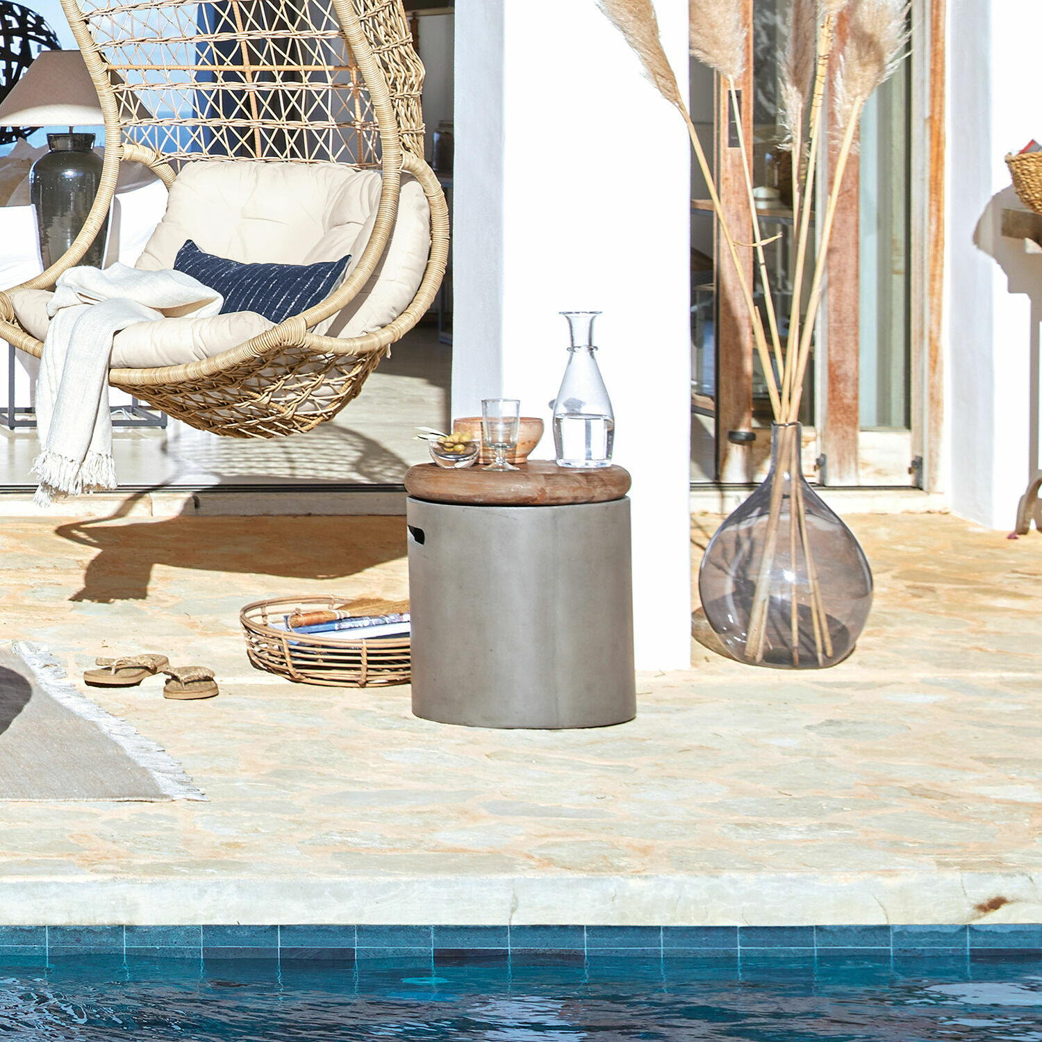 Runder Beistelltisch mit Betonsockel und Holzplatte auf Terrasse am Pool mit hängendem Rattansessel
