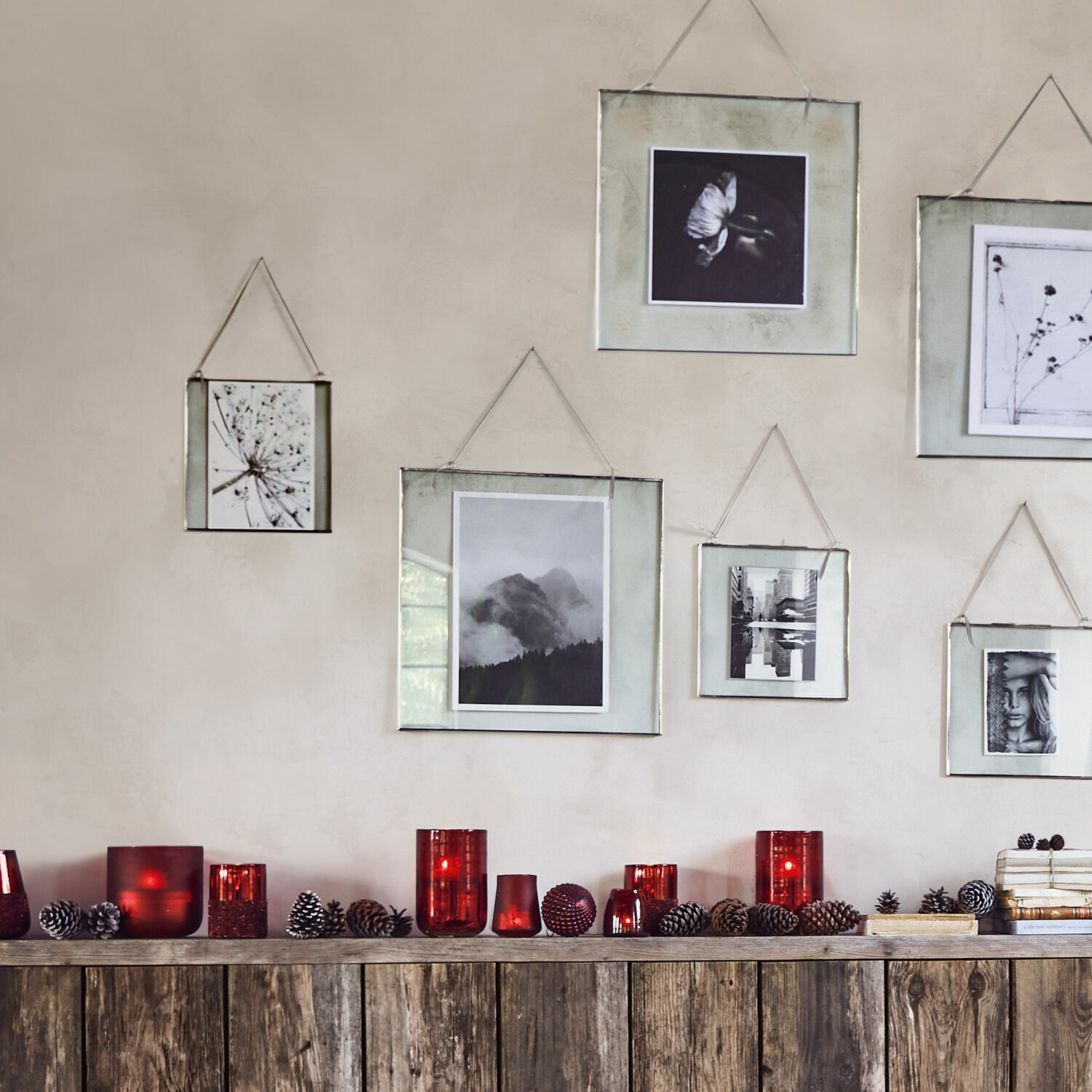 Dekorative rote Glas-Teelichthalter und Kiefernzapfen auf Holzregal unter an der Wand hängenden Bilderrahmen