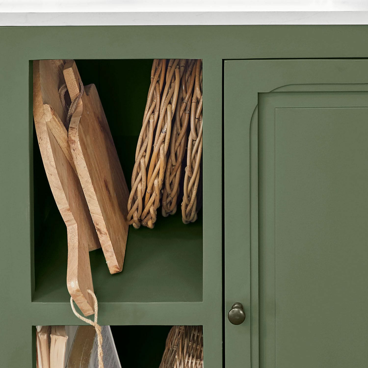 Grüner Holzschrank mit offenem Fach für Holz-Schneidebretter und geflochtene Aufbewahrungskörbe