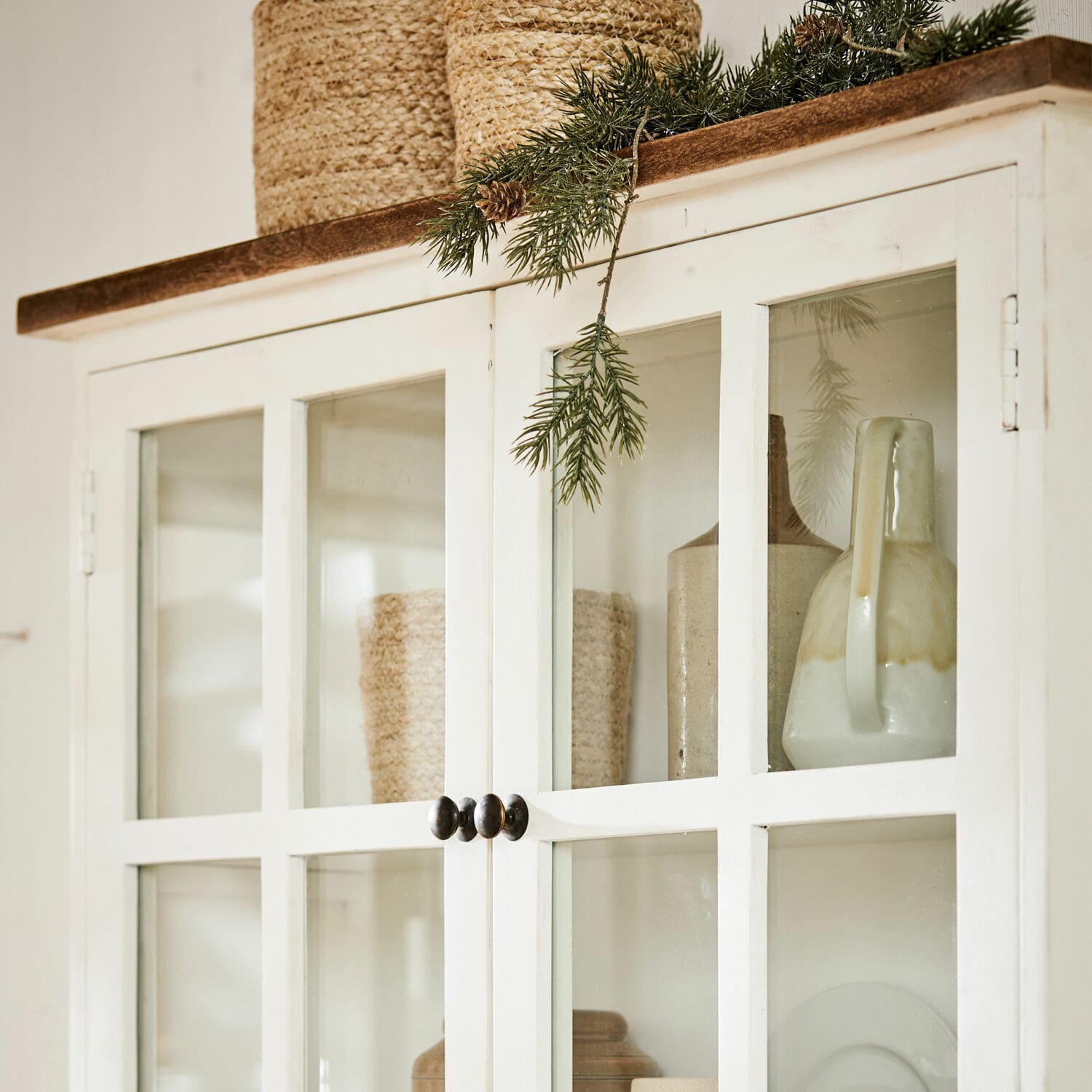 Weiße Holzvitrine mit Glastüren und grüner Tannenzweig-Dekoration oben