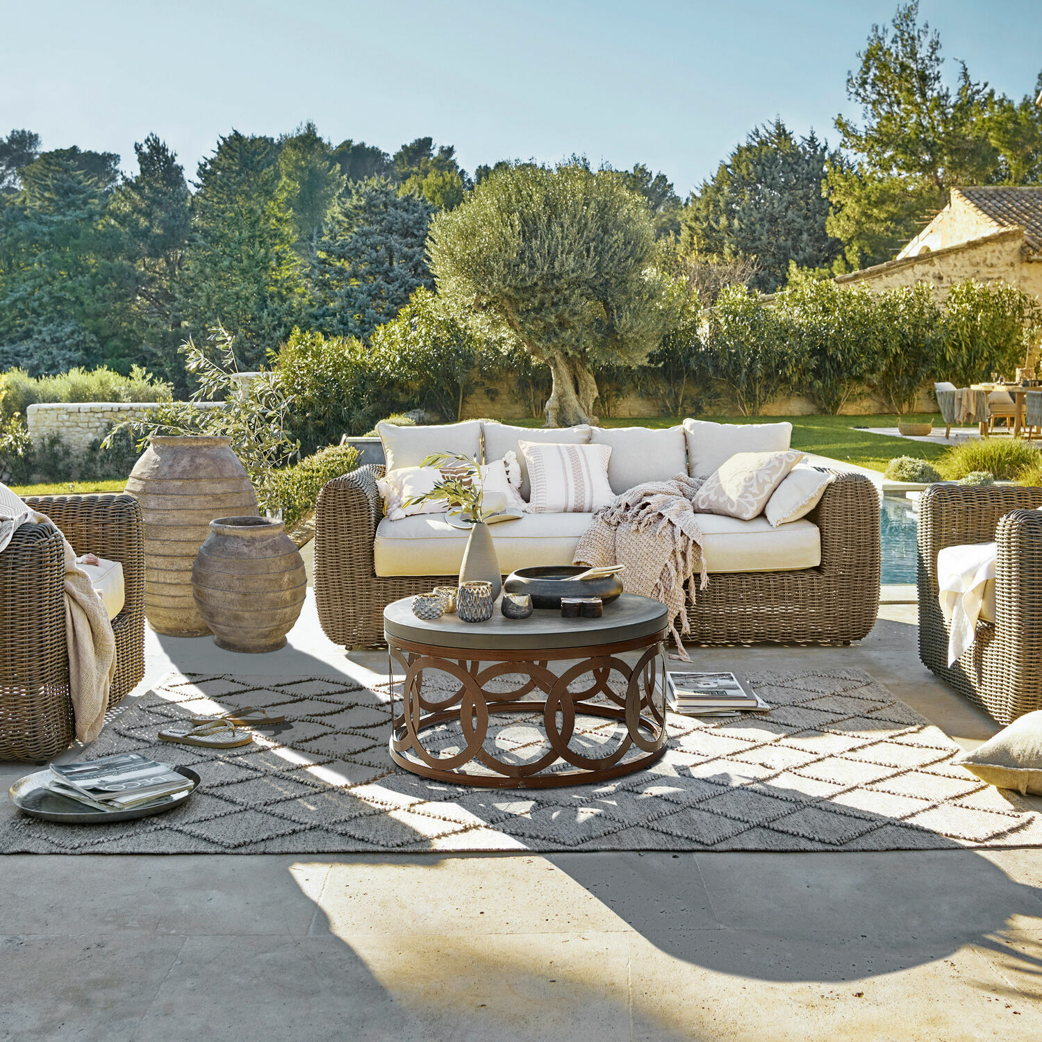 Gartenmöbel-Set aus Rattan mit hellen Kissen auf Terrasse mit Teppich und Couchtisch