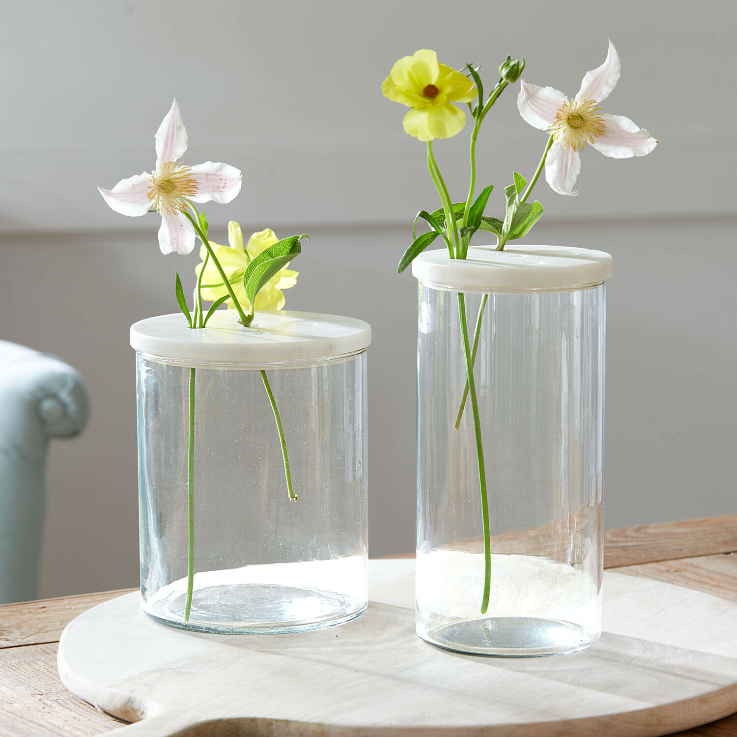 Glasdose 2er Set Rosanella Zwei transparente Glasvasen mit weißen Deckeln und hellen Blumen auf einem Holztisch