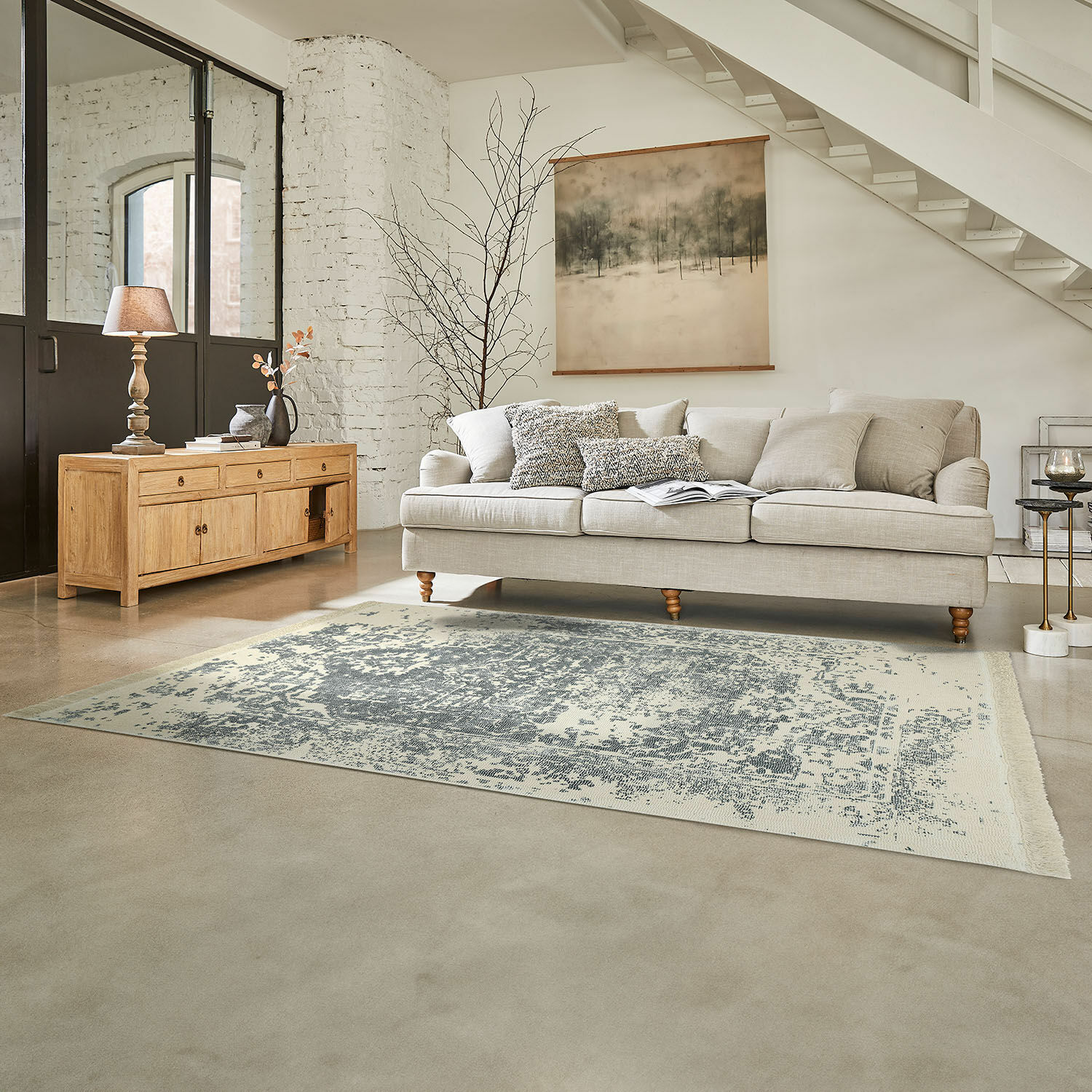 Teppich Lortet Beige Sofa mit Kissen auf grauem Teppich in hellem Wohnzimmer mit Holzkommode und Wanddekoration