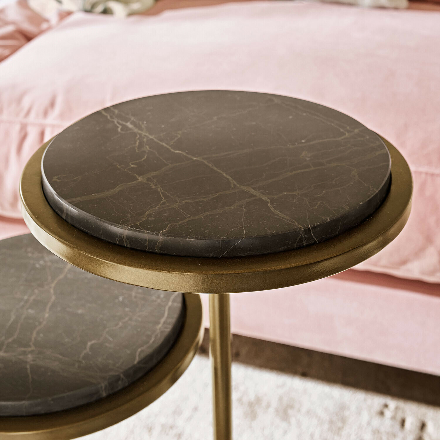 Beistelltisch mit schwarzer Marmorplatte und messingfarbenem Metallgestell vor rosa Sofa