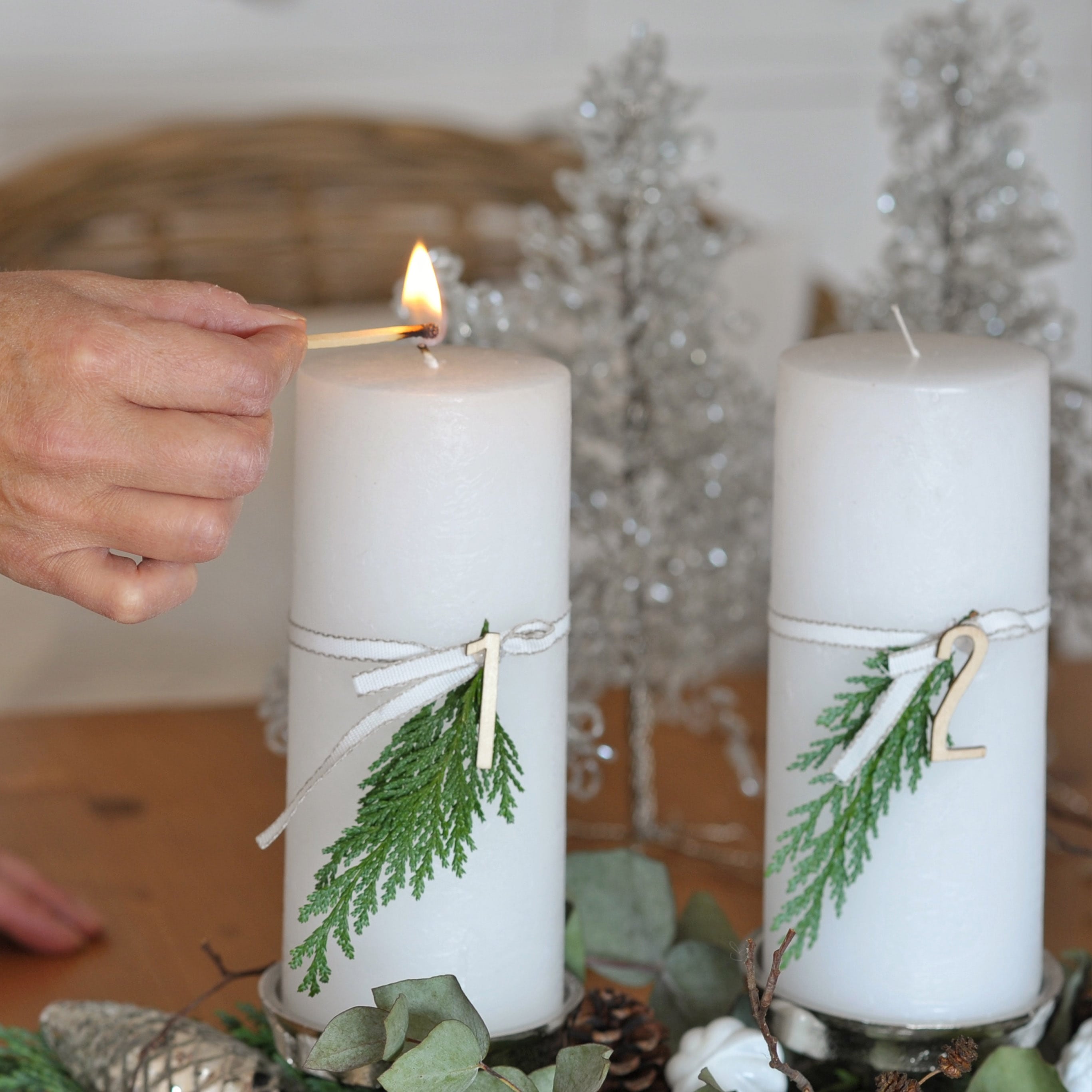 Weiße Adventskerzen mit grünen Zweigen und Holznummern auf dekorativem Weihnachtstablett