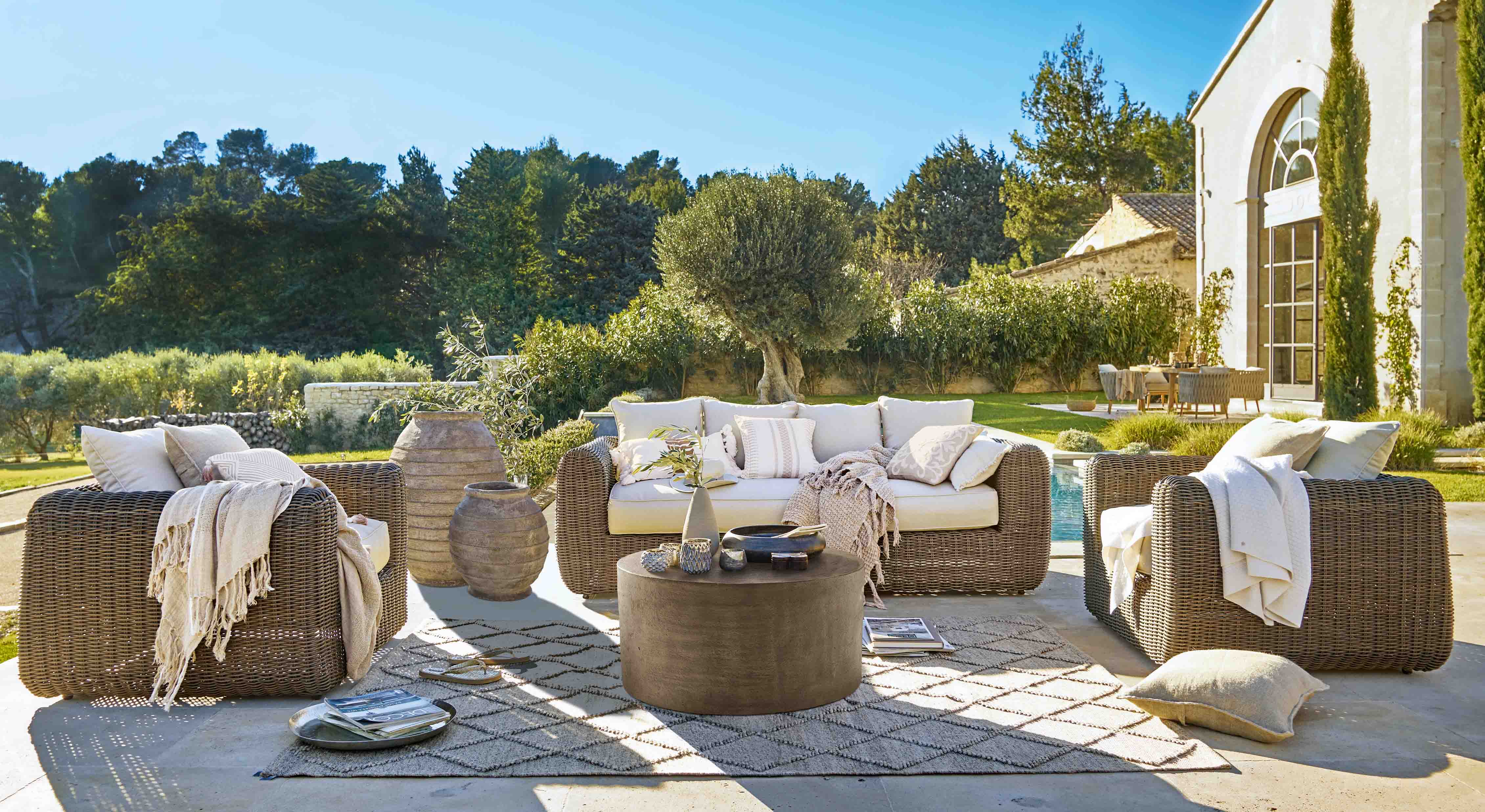 Braunes Rattan-Gartenmöbel-Set mit cremefarbenen Kissen und Dekorationen auf sonniger Terrasse