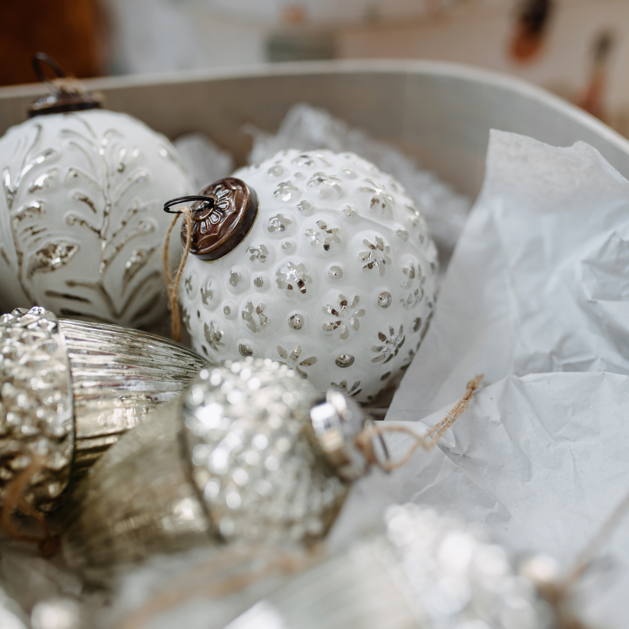 Weiße und silberne Weihnachtskugeln aus Glas und Metall mit Mustern in einer Schachtel mit Papier