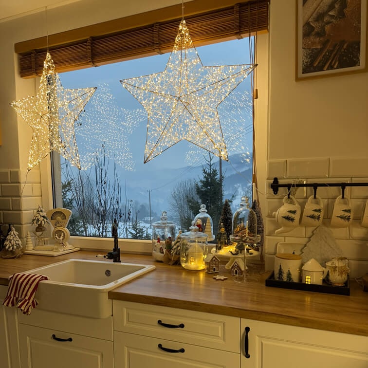 Leuchtende Stern-Dekorationen in der Küche mit Holzarbeitsplatte und Weihnachtsdeko vor winterlicher Aussicht