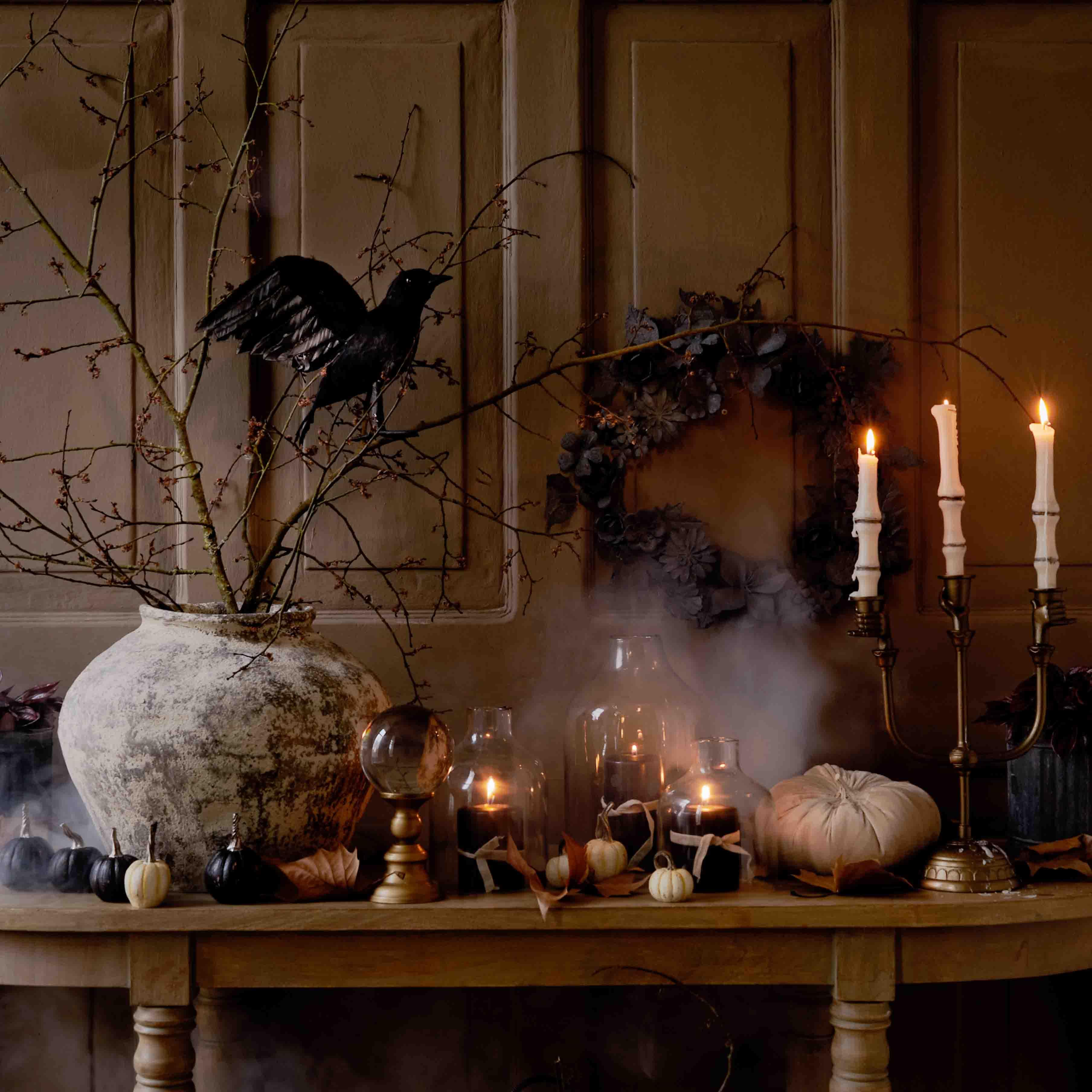 Herbstliche Tischdekoration mit großem Keramikvase, brennenden Kerzen und schwarzem Vogel auf Zweig