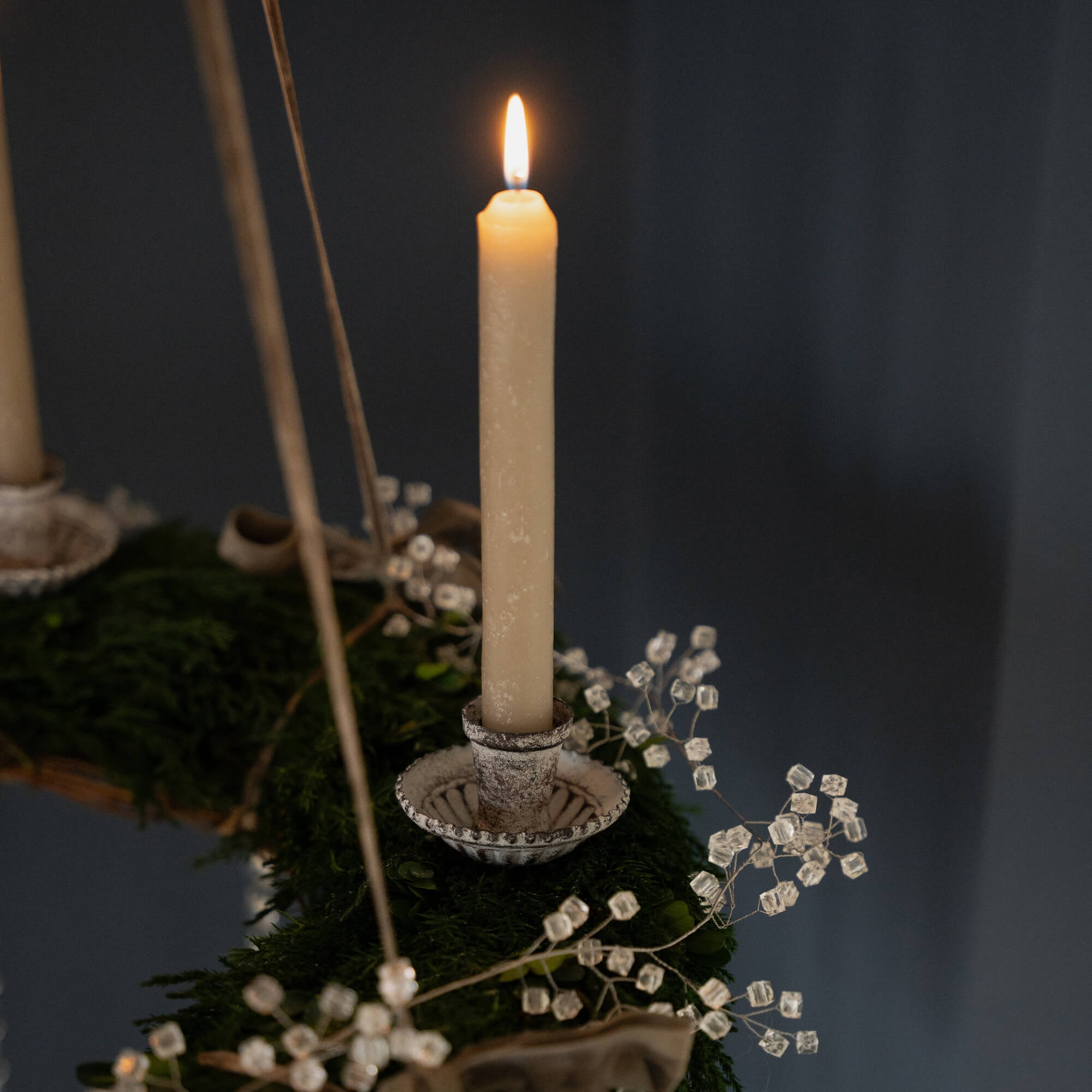 Detail einer brennenden Kerze auf grünem Adventskranz mit Kristalldekor vor dunklem Hintergrund
