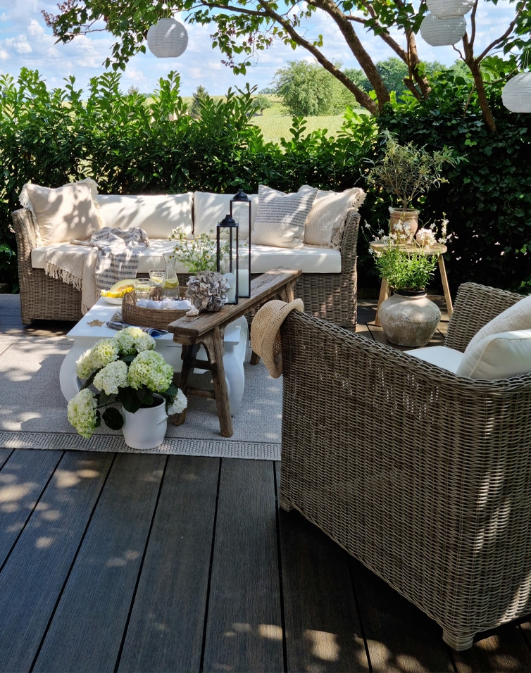 Gemütliche Gartenmöbel aus Rattan mit beigen Kissen auf Terrasse mit Blumen und Laternen dekoriert