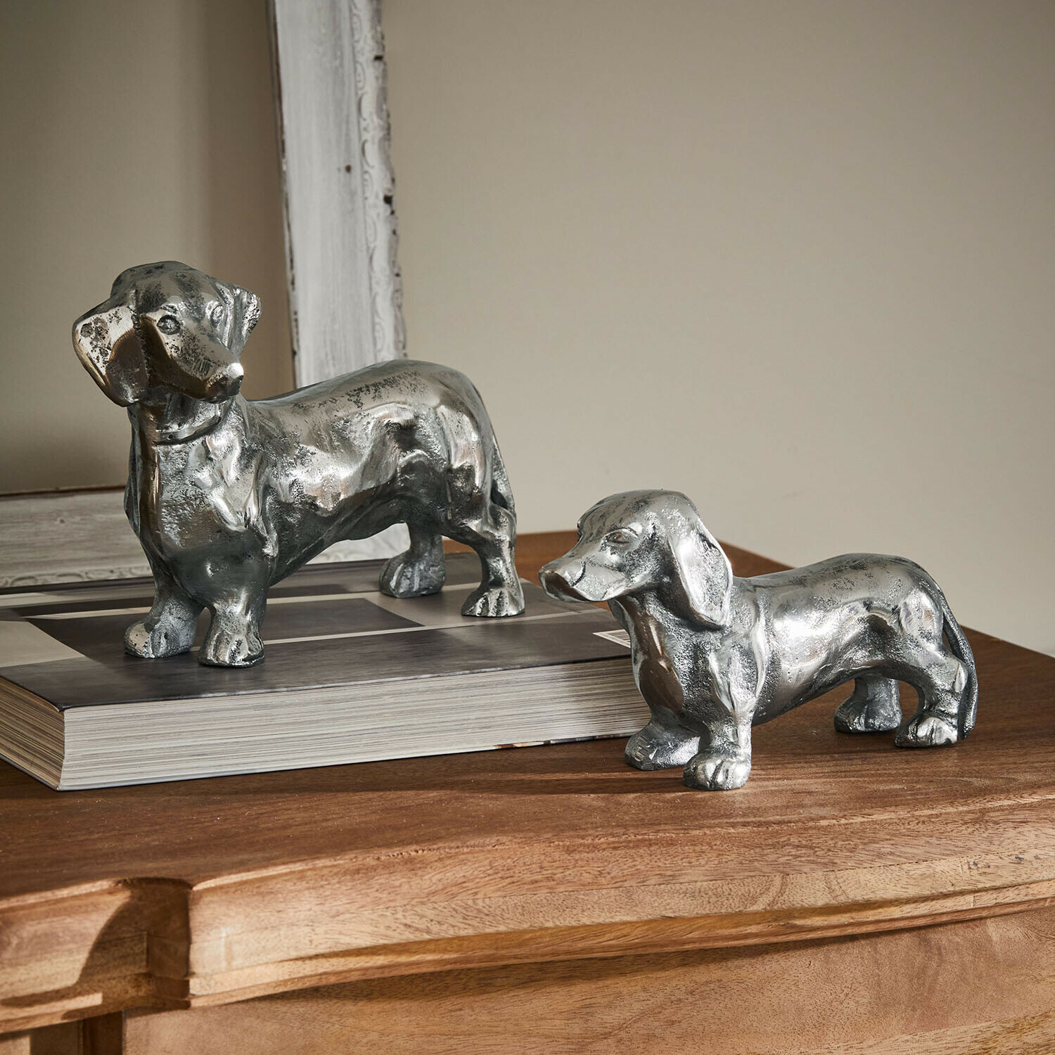 Deko-Hund 2er Set Calwen Zwei silberne Dackel-Figuren aus Metall auf einem Holztisch als stilvolle Wohnaccessoires
