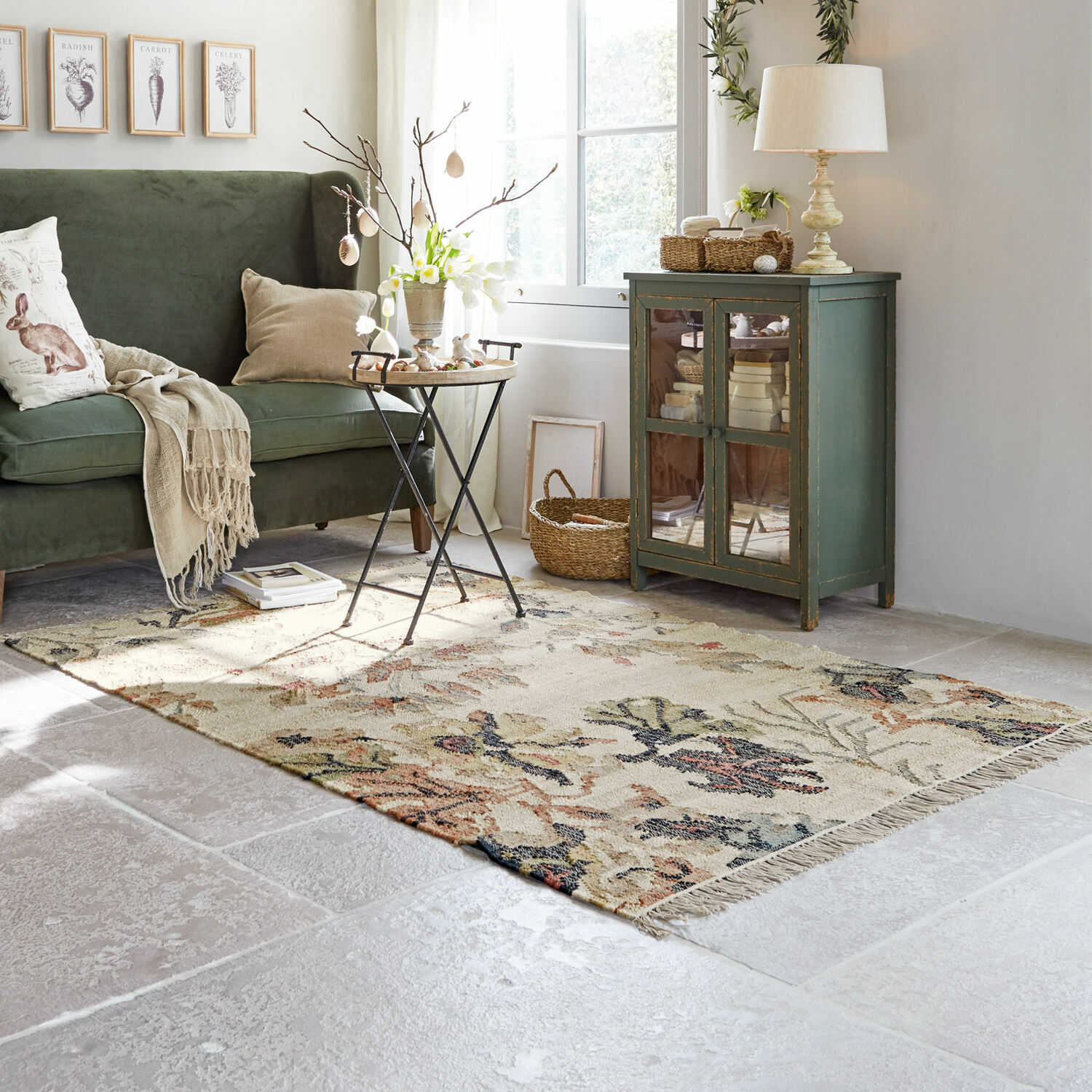 Teppich Osorno Gemütliches Wohnzimmer mit grünem Sofa, beigem Teppich mit Blumenmuster und vintage Holzschrank