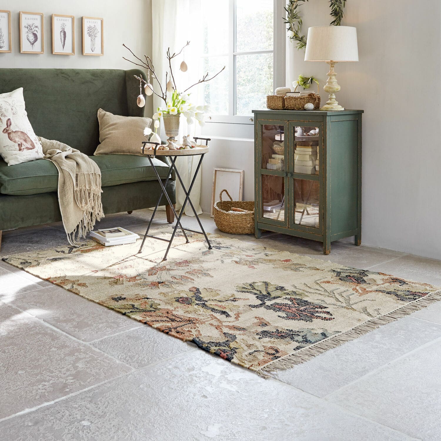 Teppich Osorno Gemütliches Wohnzimmer mit grünem Sofa, beigem Teppich mit Blumenmuster und vintage Holzschrank