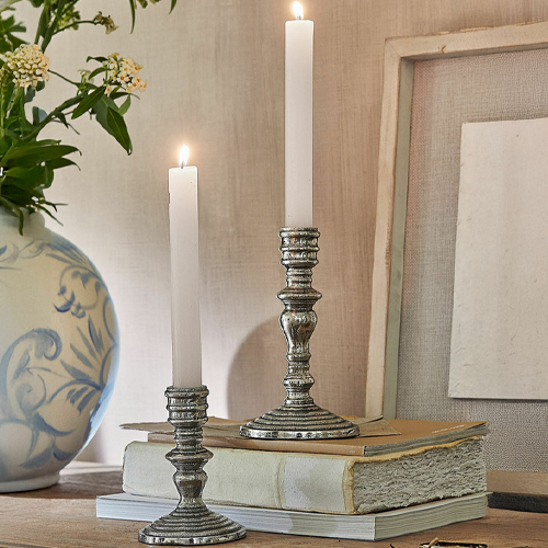 Zwei Metallkerzenhalter mit weißen Kerzen auf alten Büchern auf einem Holztisch