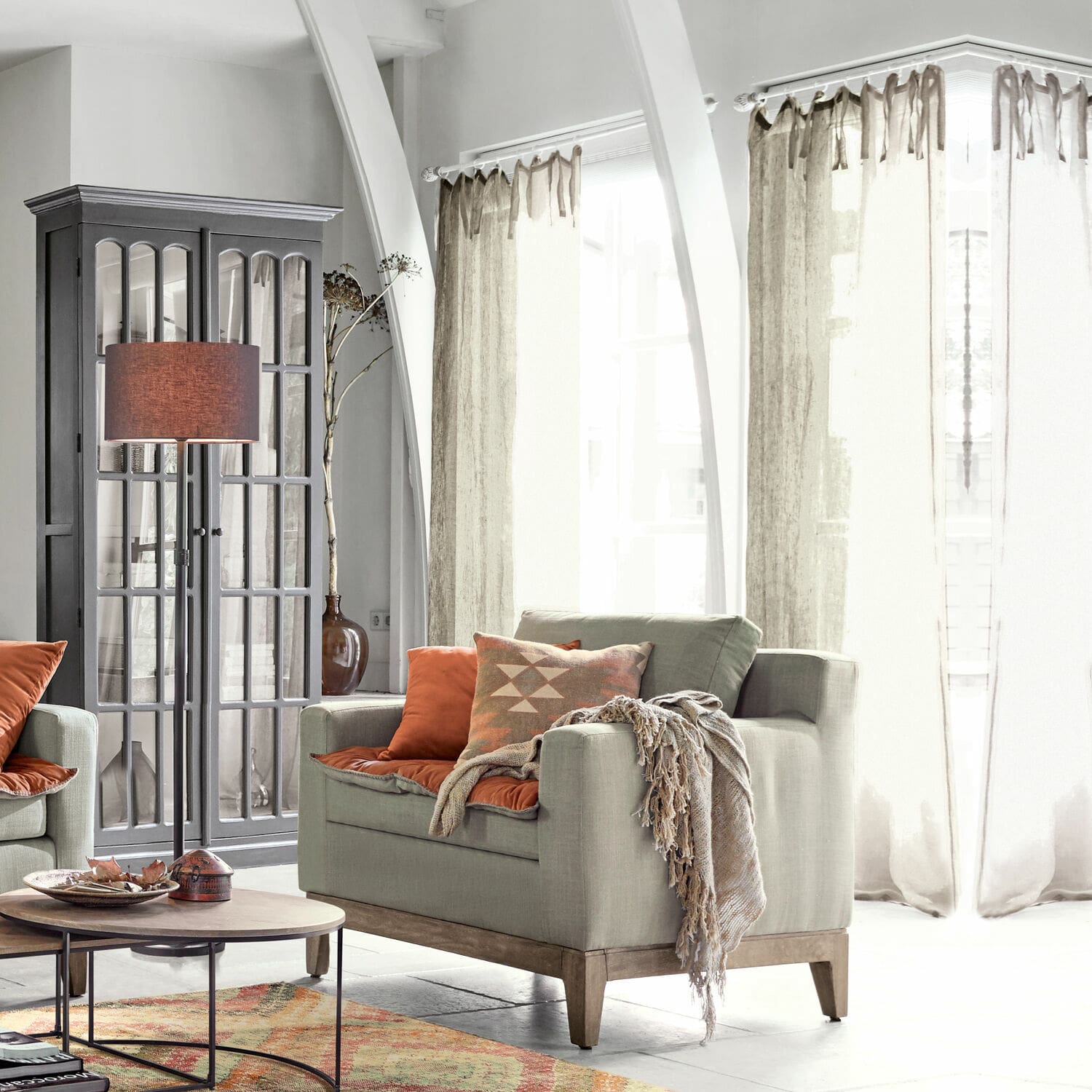 Graues Sofa mit Holzsockel und orangefarbenen Kissen in hellem Wohnzimmer mit Stehlampe
