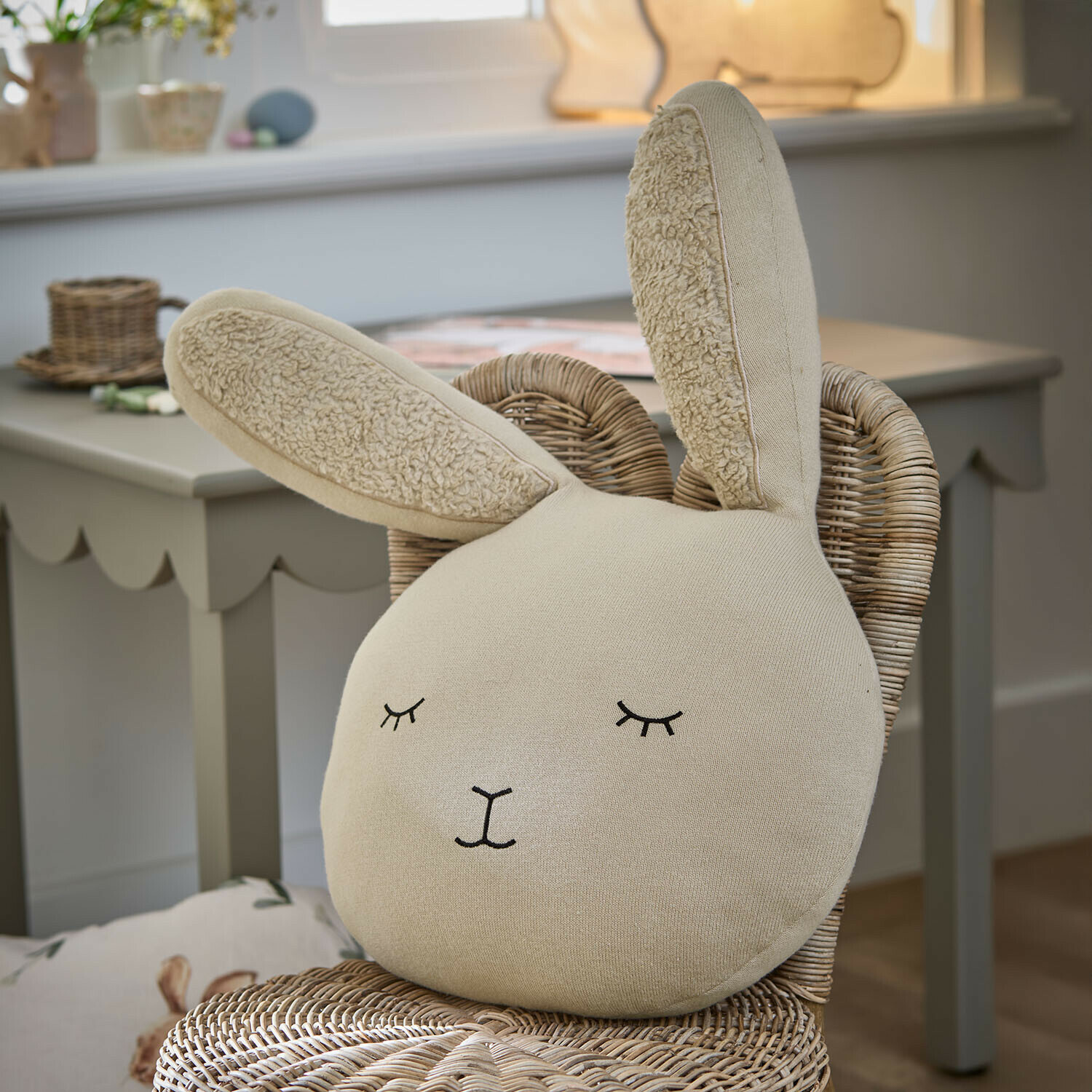 Kissen Fuzzletop Beiges Hasenkissen aus weichem Stoff auf einem Rattanstuhl im Kinderzimmer