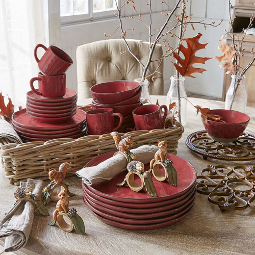 Rotes Keramik-Geschirrset mit Tassen und Tellern im Weidenkorb, herbstliche Dekoration