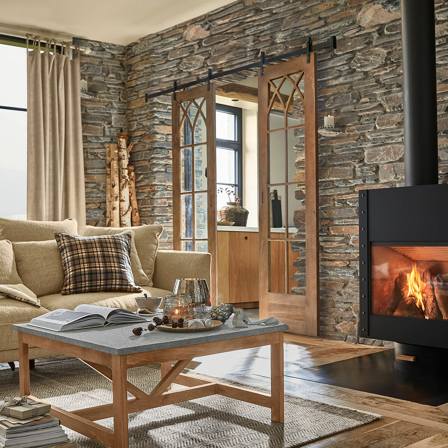 Wohnzimmer mit Steinwand, Holztisch mit grauer Tischplatte und brennendem Kamin