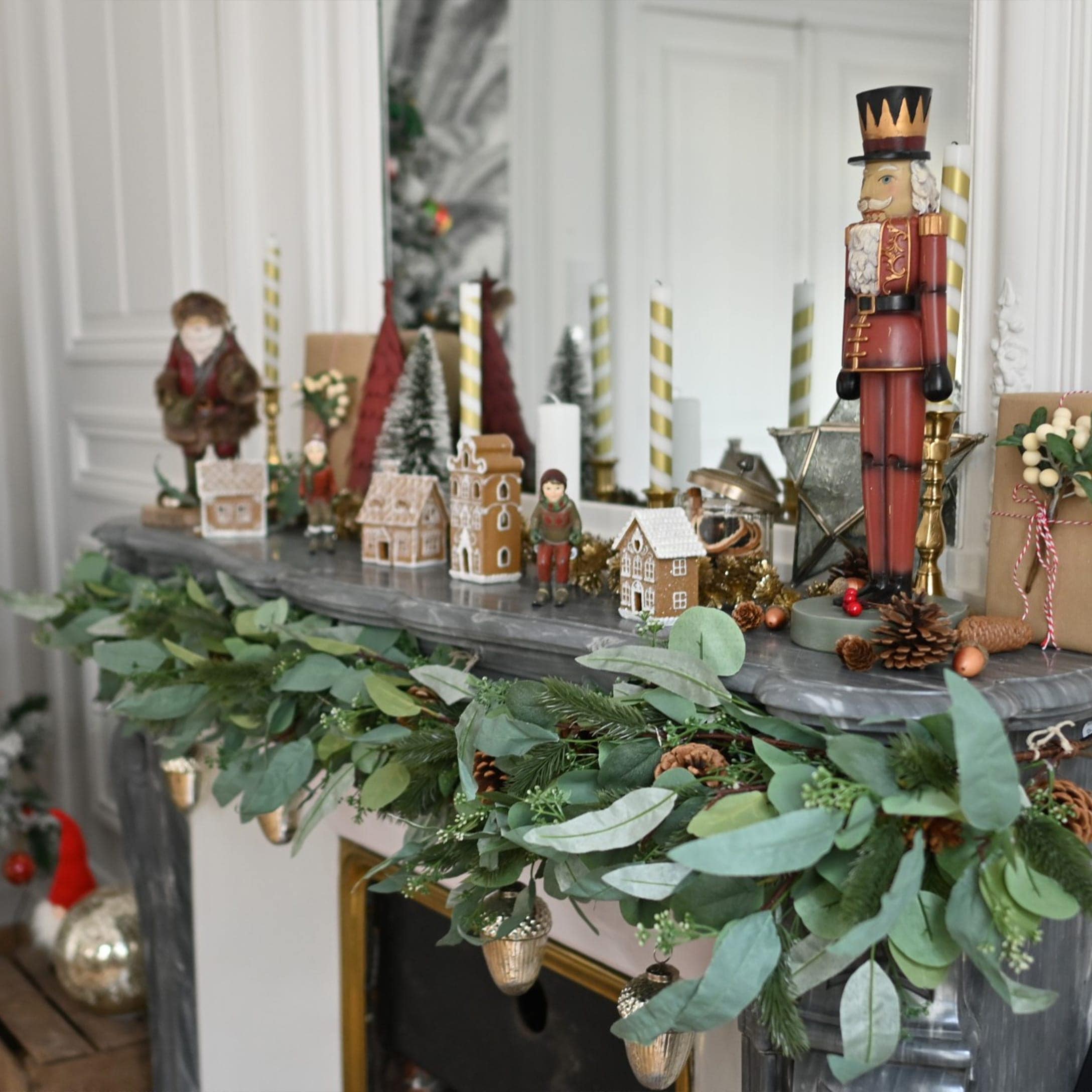 Weihnachtliche Kamindekoration mit grünen Zweigen, Zapfen und Nussknackerfigur auf grauem Marmor