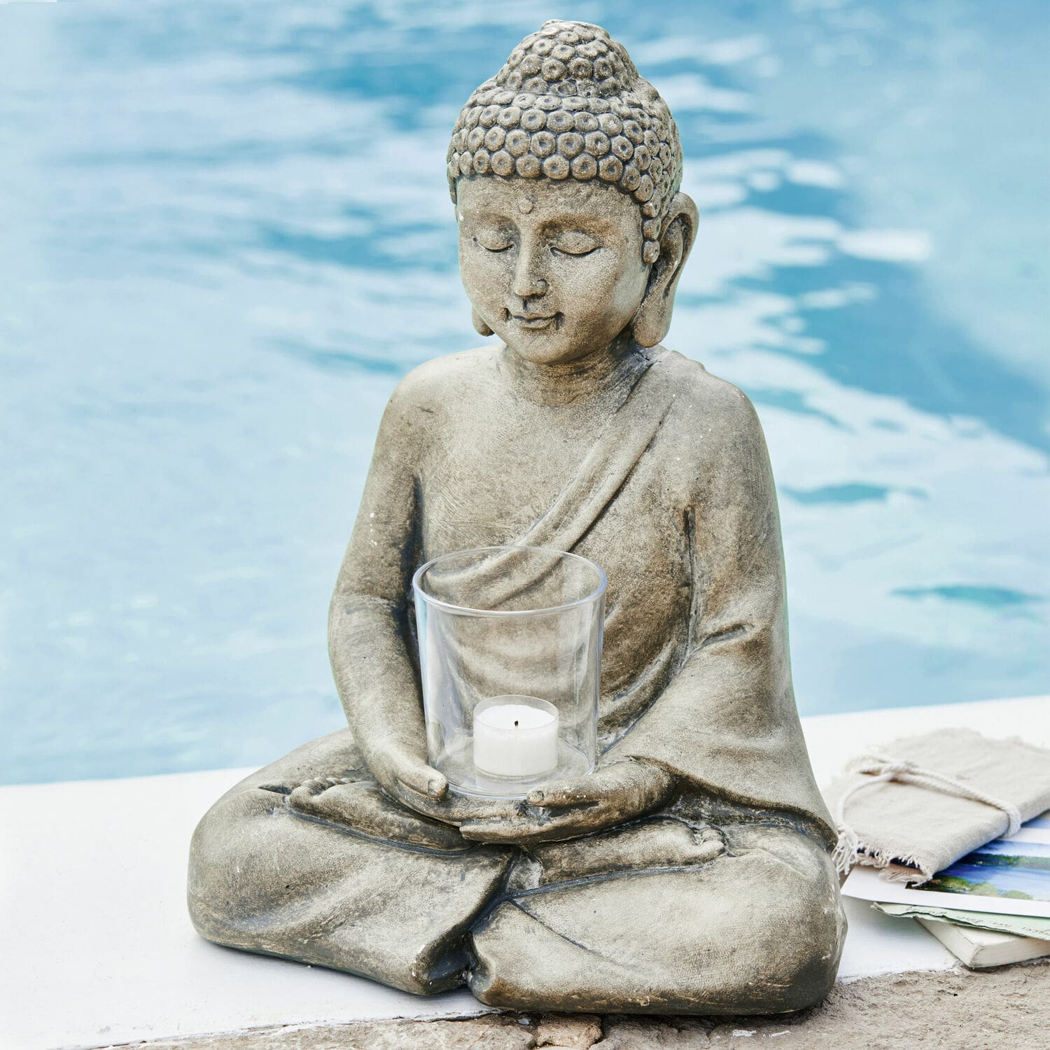 Windlicht Sylvain Graue Buddha-Figur aus Stein mit klarem Teelichthalter am Poolrand für entspannte Atmosphäre